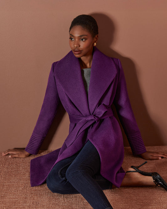 Front view of model wearing a Sentaler mid length dark mulberry coat made of baby alpaca wool, with a shawl collar, worn belted