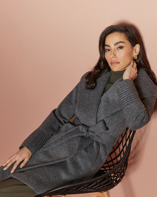 Side view of model wearing a Sentaler mid length grey mélange coat made of baby alpaca wool, with a shawl collar, worn belted.