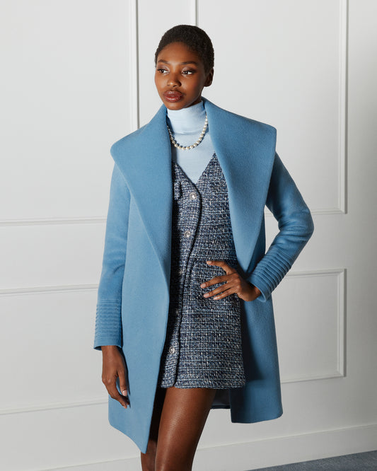 Front view of model wearing a Sentaler mid length steel blue coat made of baby alpaca wool, with a shawl collar, worn open.