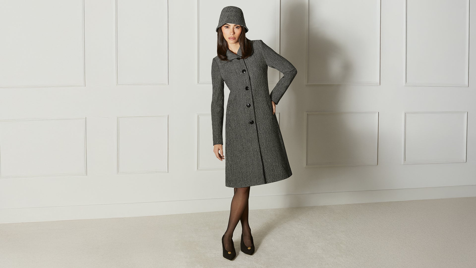 Front view of model wearing a Sentaler black, gold and ivory A-line coat made of tweed suri alpaca wool, worn buttoned, with black, gold, and ivory alpaca bucket hat.