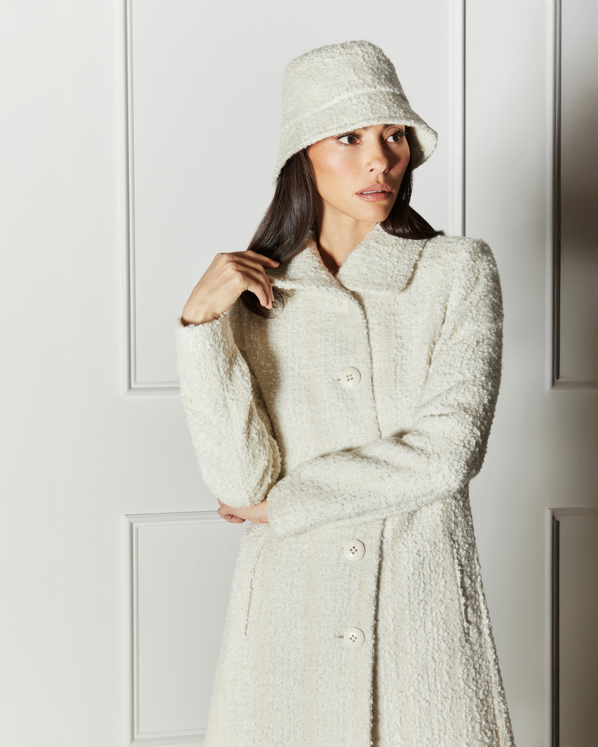 Front view of model wearing a Sentaler ivory glittered A-line coat made of tweed suri alpaca wool, worn buttoned, with matching ivory tweed bucket hat.