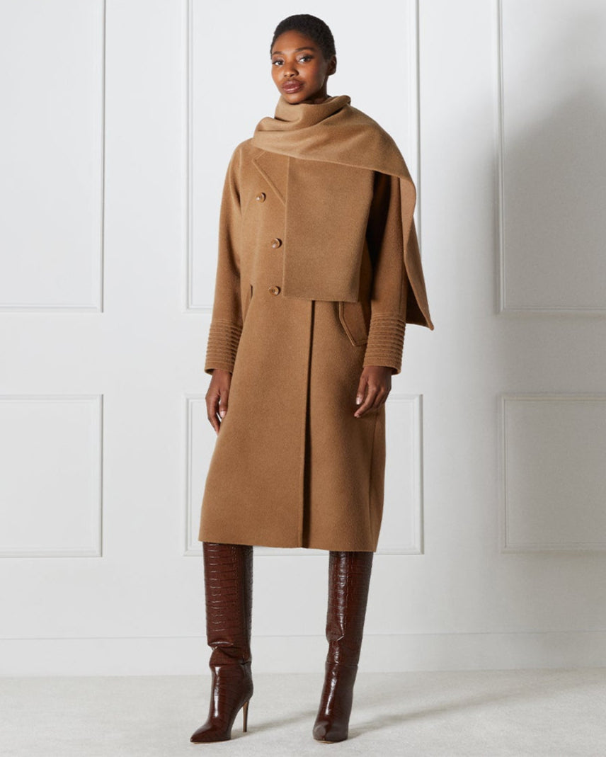 Front view of model wearing a Sentaler dark camel double breasted coat made of baby alpaca wool with a notched collar, worn with fabric scarf, closed.