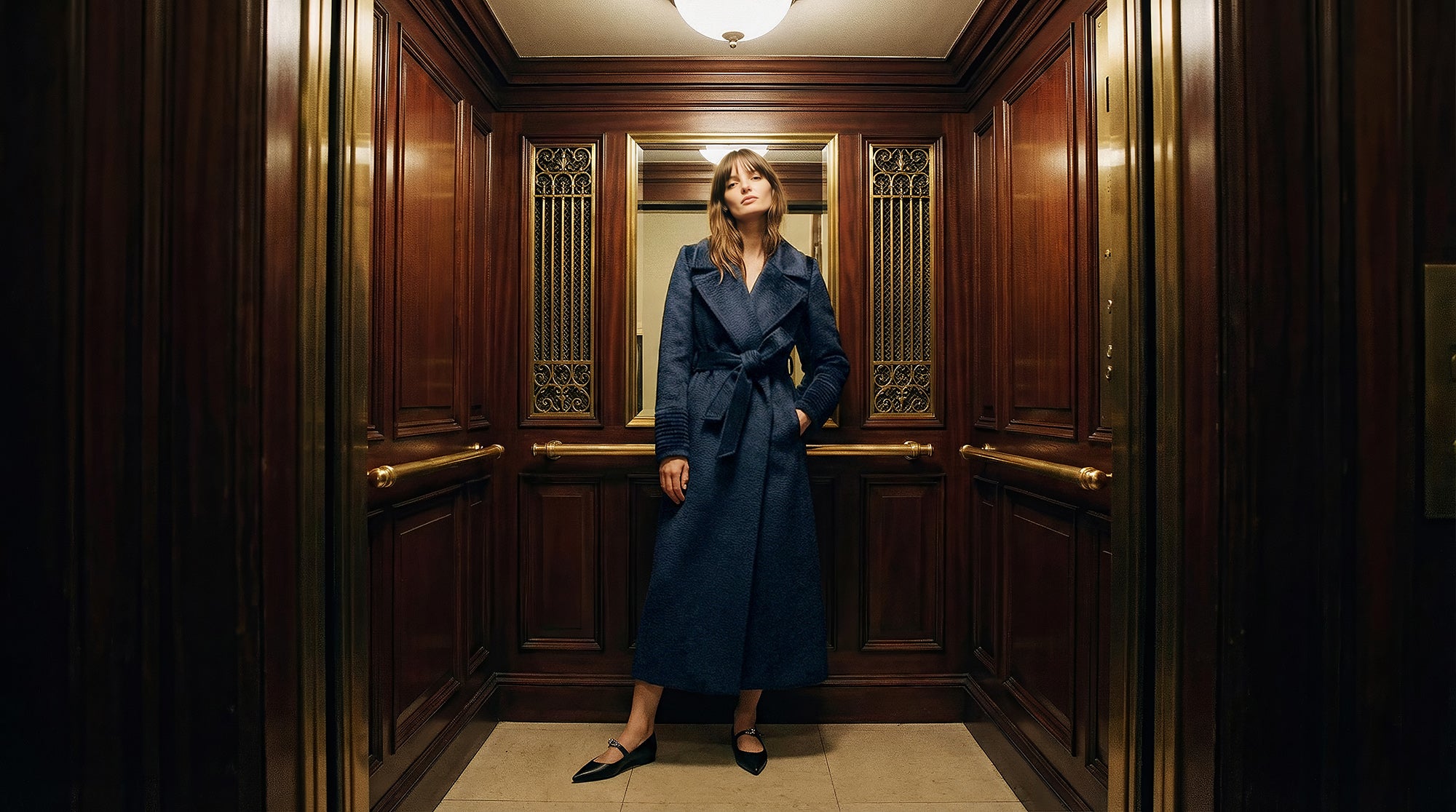 Front view of model wearing a Sentaler deep navy maxi coat made of suri alpaca wool, with a notched collar, worn belted.