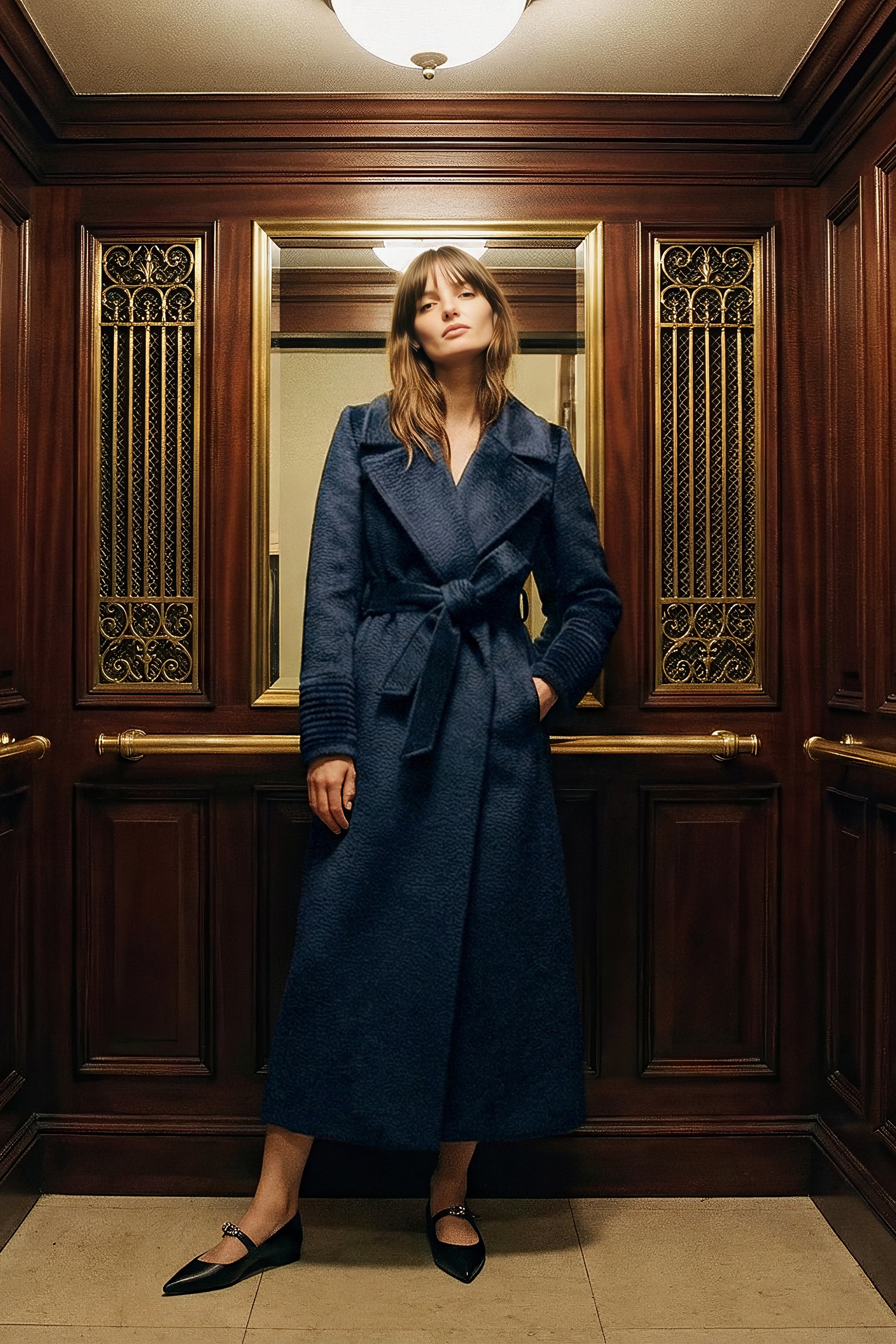 Front view of model wearing a Sentaler deep navy maxi coat made of suri alpaca wool, with a notched collar, worn belted.