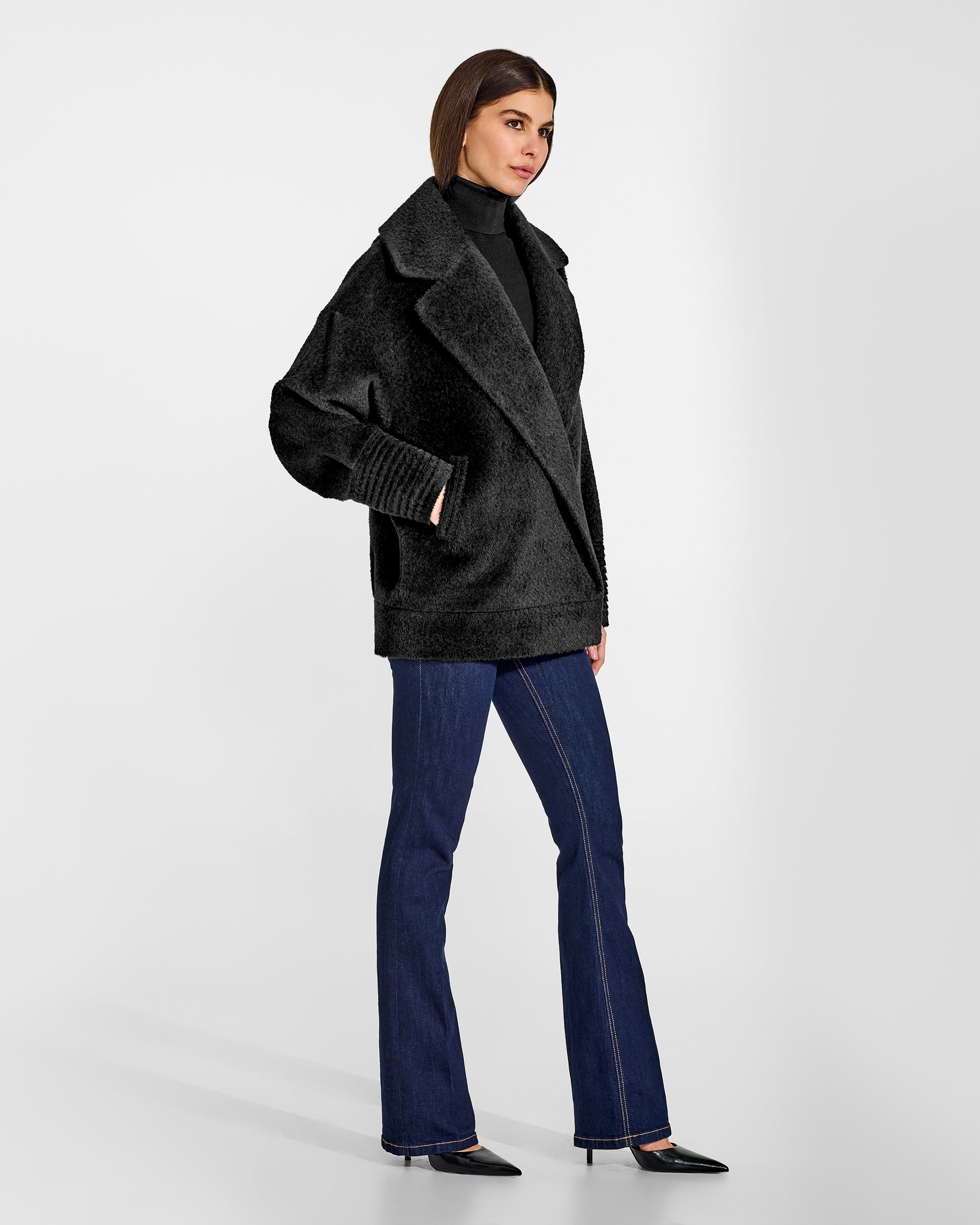 Side view of model wearing a Sentaler black aviator jacket made of bouclé alpaca wool, with dropped shoulders, worn buttoned.