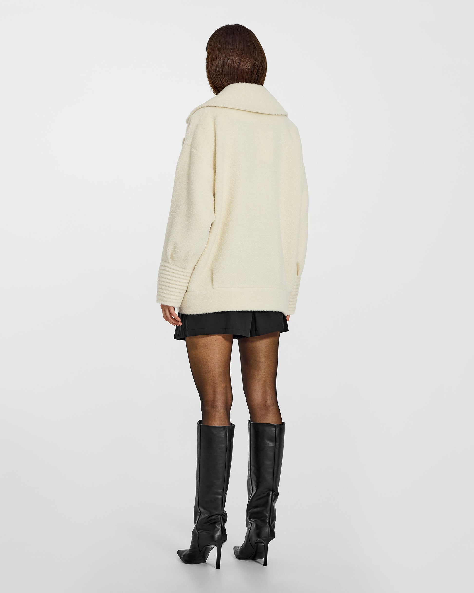 Back view of model wearing a Sentaler ivory aviator jacket made of bouclé alpaca wool, with dropped shoulders, worn buttoned.