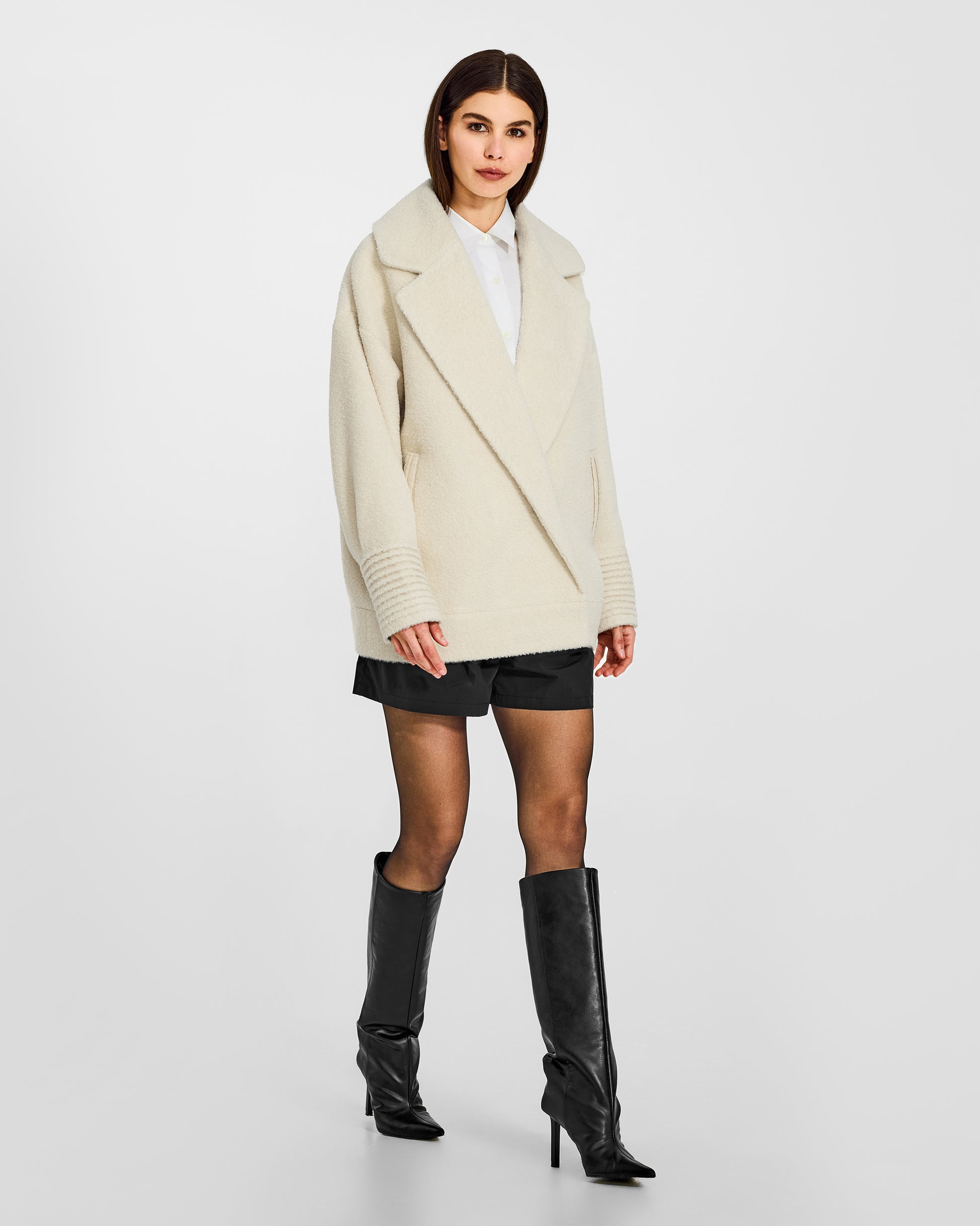 Side view of model wearing a Sentaler ivory aviator jacket made of bouclé alpaca wool, with dropped shoulders, worn buttoned.