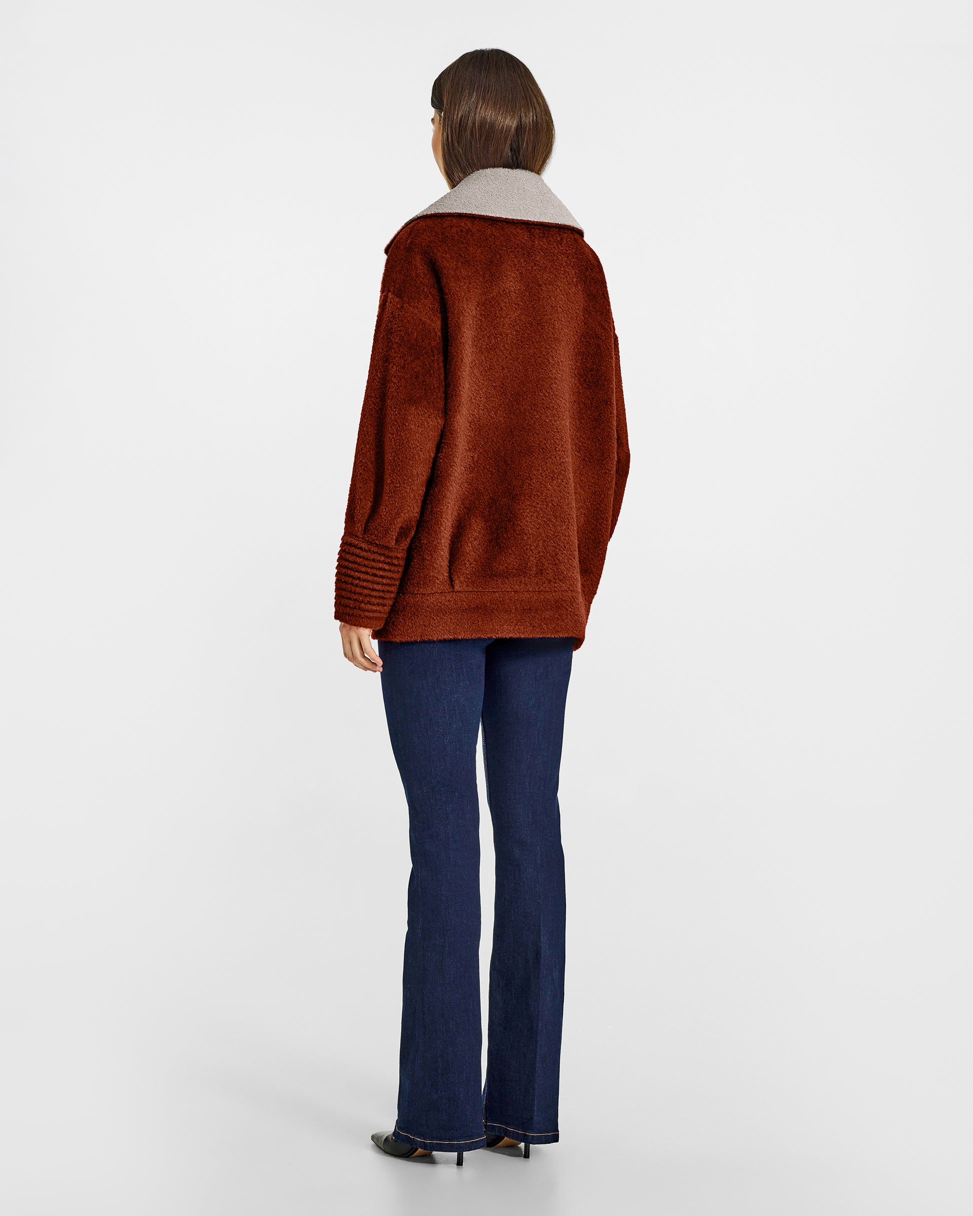 Back view of model wearing a Sentaler rust brown and sand beige aviator jacket made of bouclé alpaca wool, with dropped shoulders, worn buttoned.