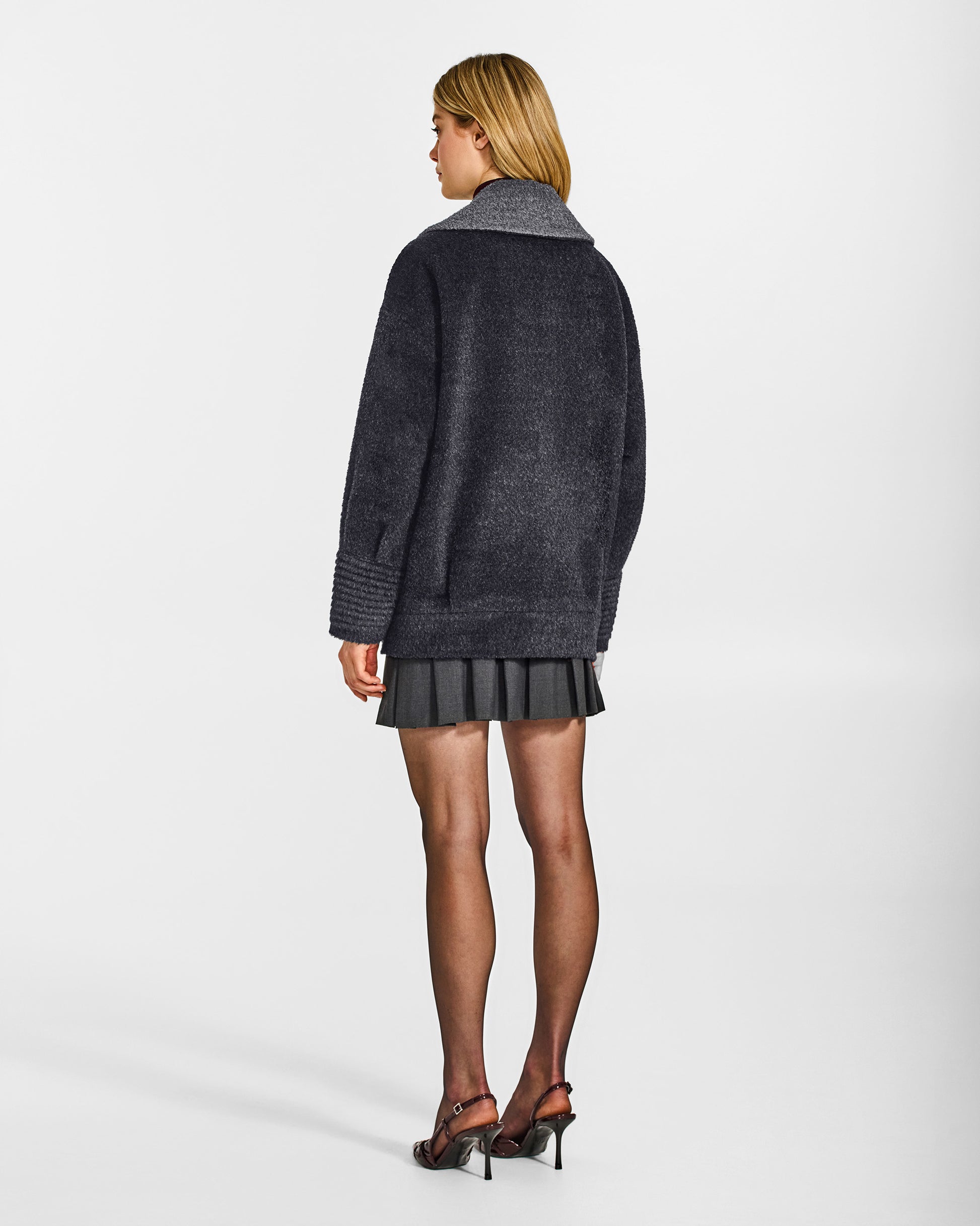 Back view of model wearing a Sentaler charcoal and grey mélange aviator jacket made of bouclé alpaca wool, with dropped shoulders, worn buttoned.
