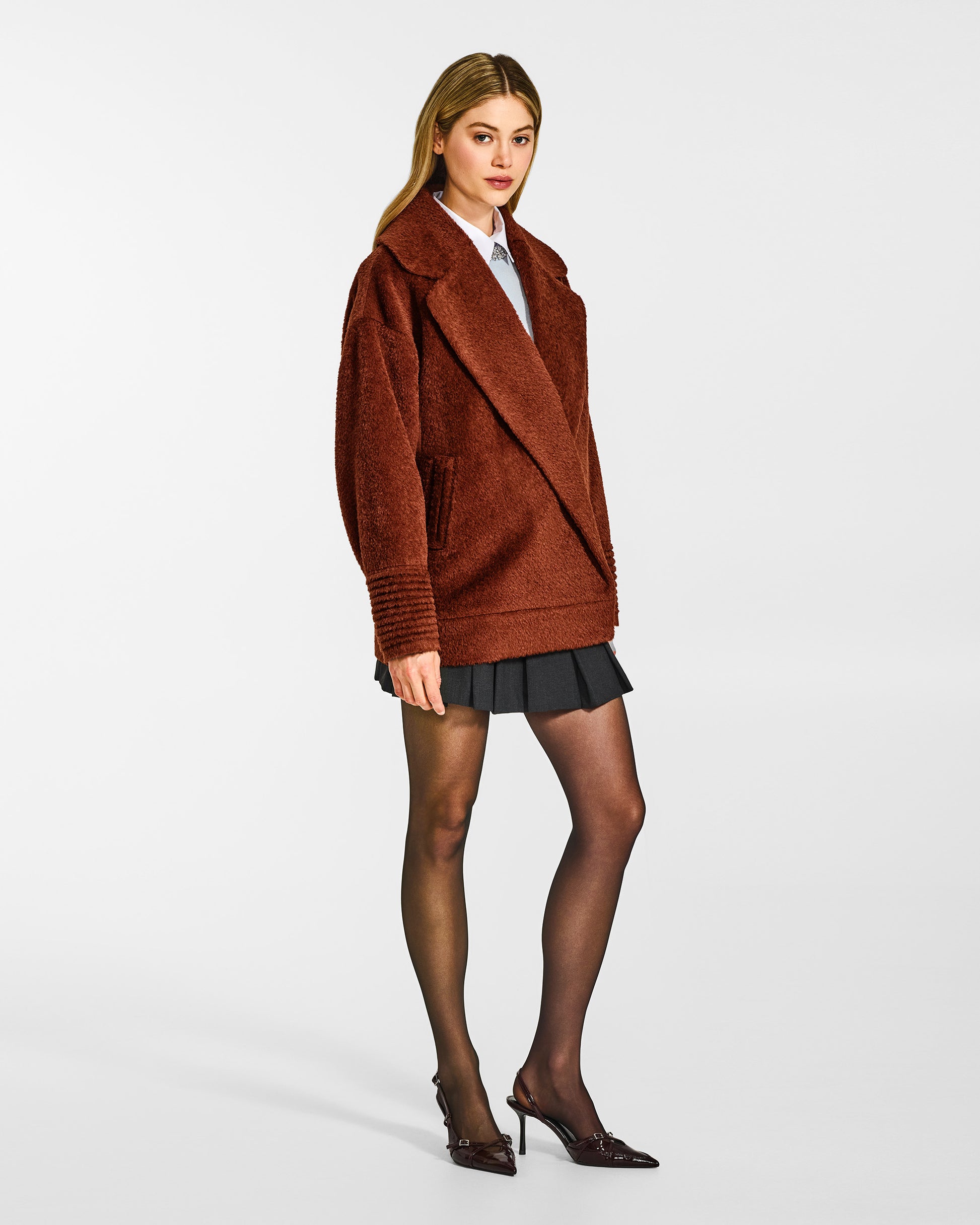Side view of model wearing a Sentaler rust brown aviator jacket made of bouclé alpaca wool, with dropped shoulders, worn buttoned.