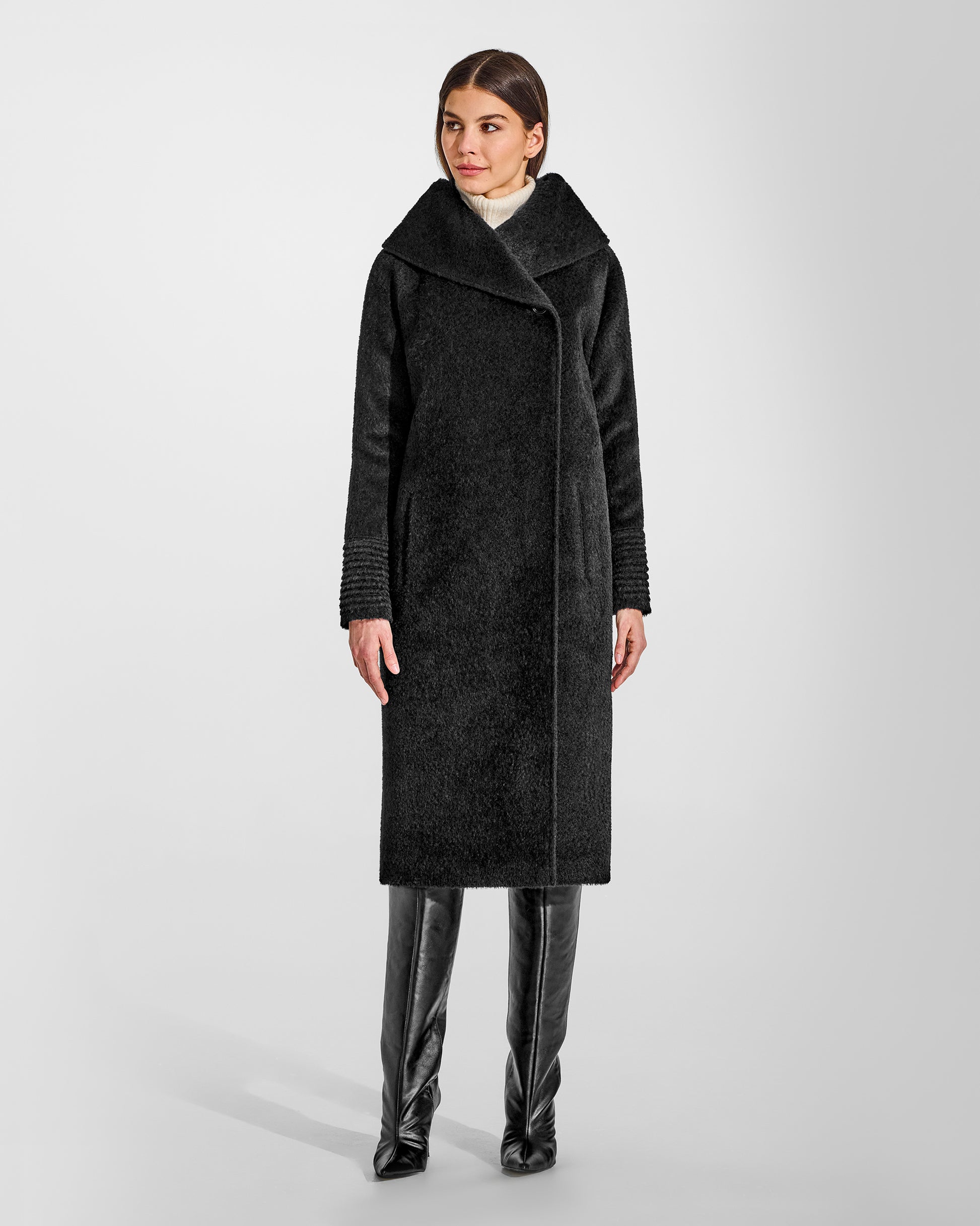 Front view of model wearing a Sentaler long black coat made of bouclé alpaca wool, with a hooded collar, worn buttoned.