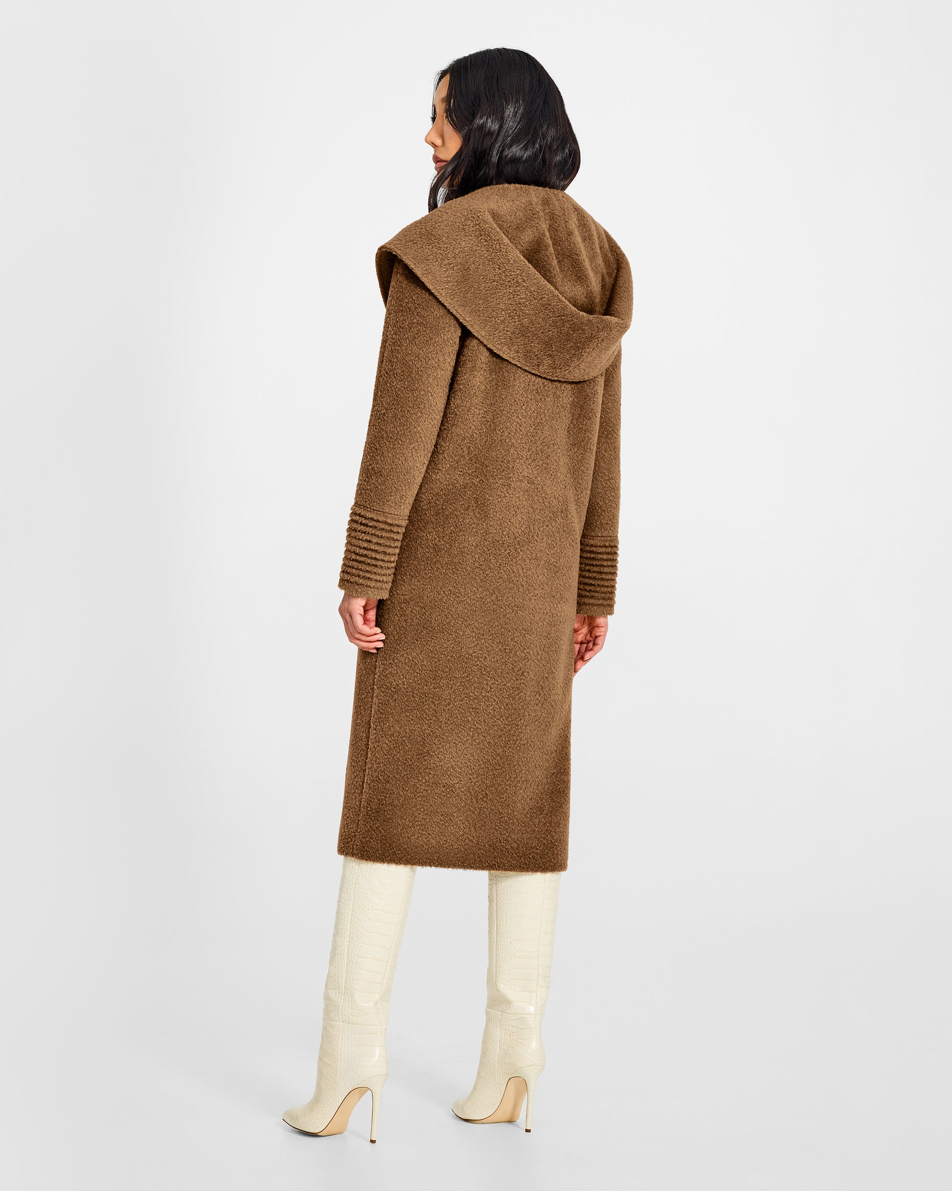Back view of model wearing a Sentaler long dark camel coat made of bouclé alpaca wool, with a hooded collar, worn buttoned.