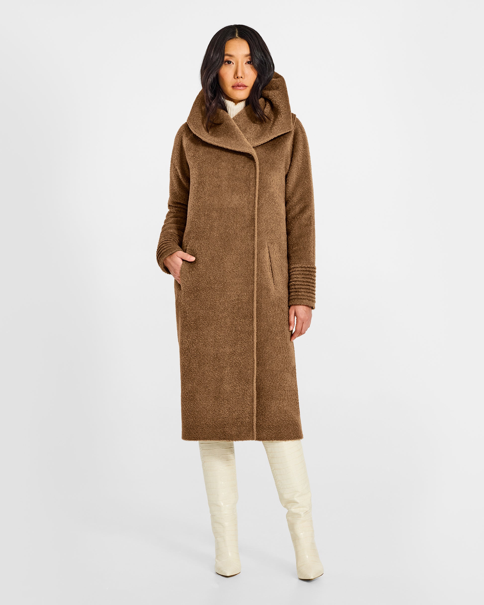 Front view of model wearing a Sentaler long dark camel coat made of bouclé alpaca wool, with a hooded collar, worn buttoned.