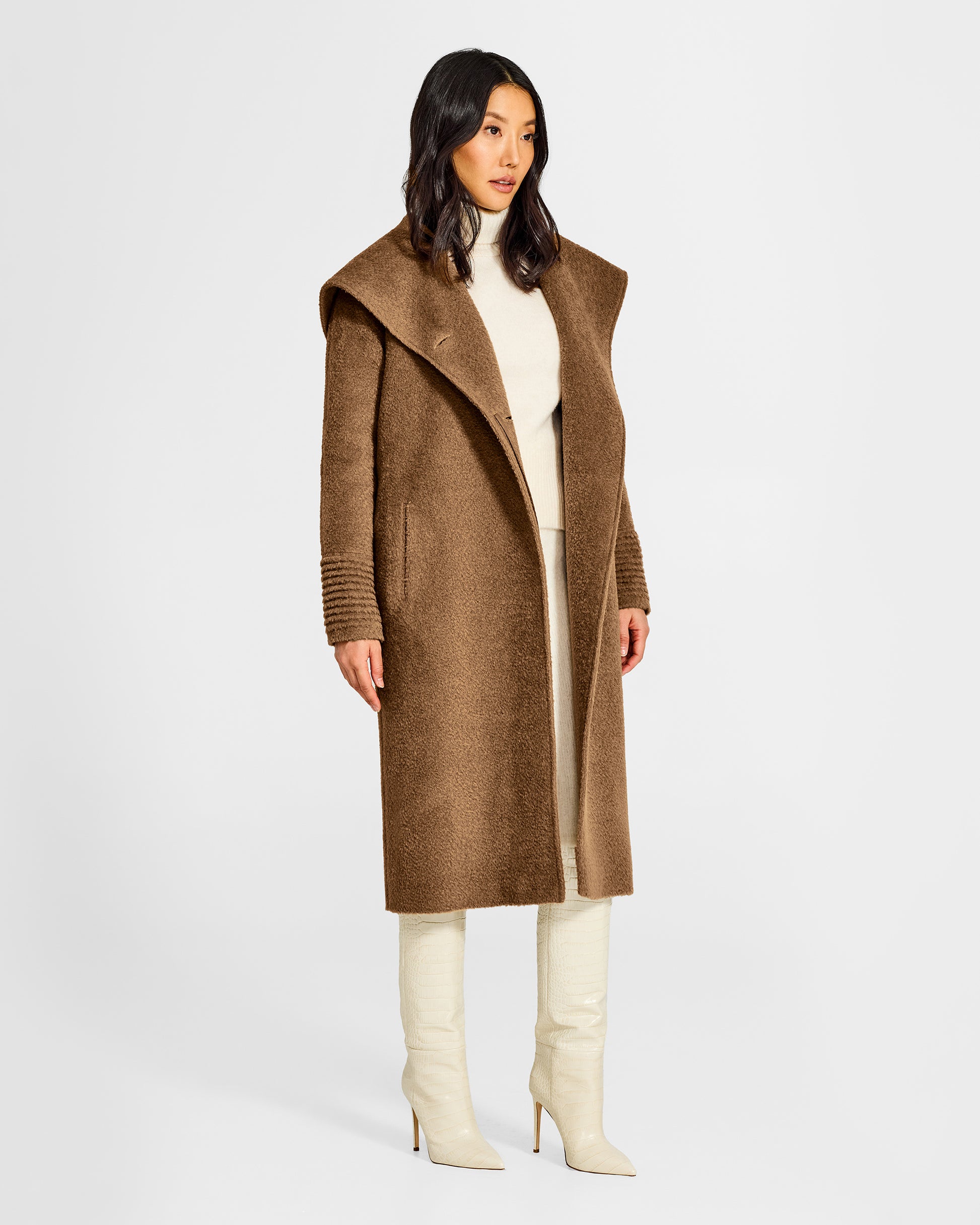Side view of model wearing a Sentaler long dark camel coat made of bouclé alpaca wool, with a hooded collar, worn open.