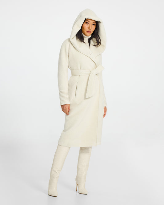 Front view of model wearing a Sentaler long ivory coat made of bouclé alpaca wool, with a hooded collar, worn belted.