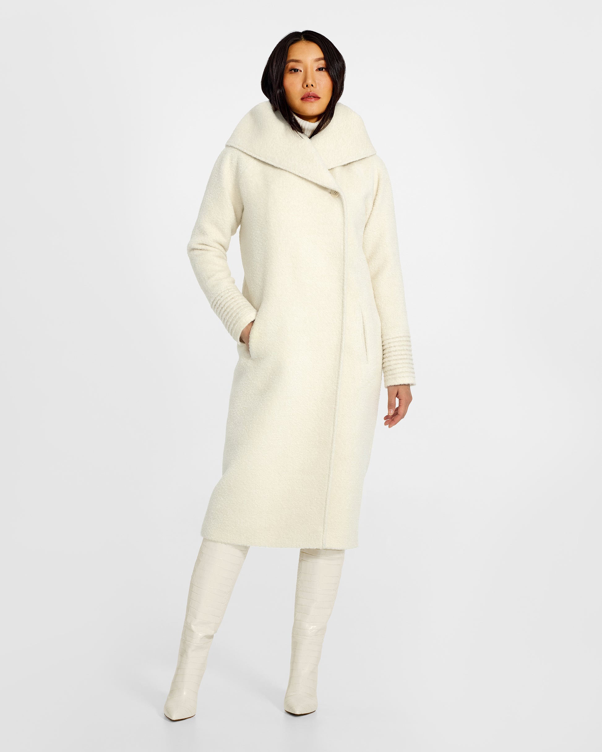 Front view of model wearing a Sentaler long ivory coat made of bouclé alpaca wool, with a hooded collar, worn buttoned.