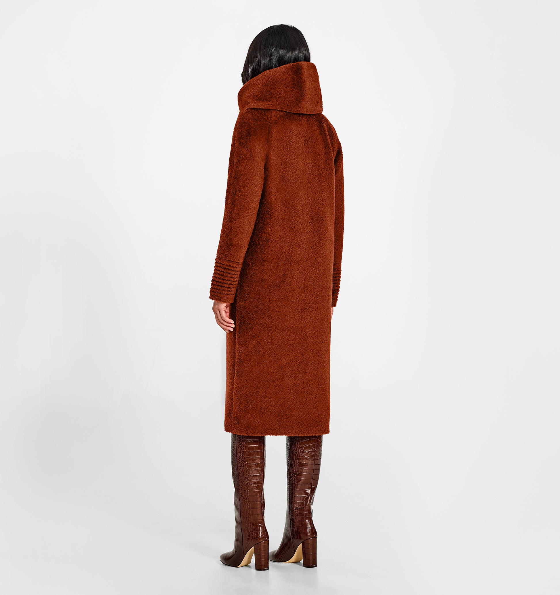 Back view of model wearing a Sentaler long rust brown coat made of bouclé alpaca wool, with a hooded collar, worn buttoned.
