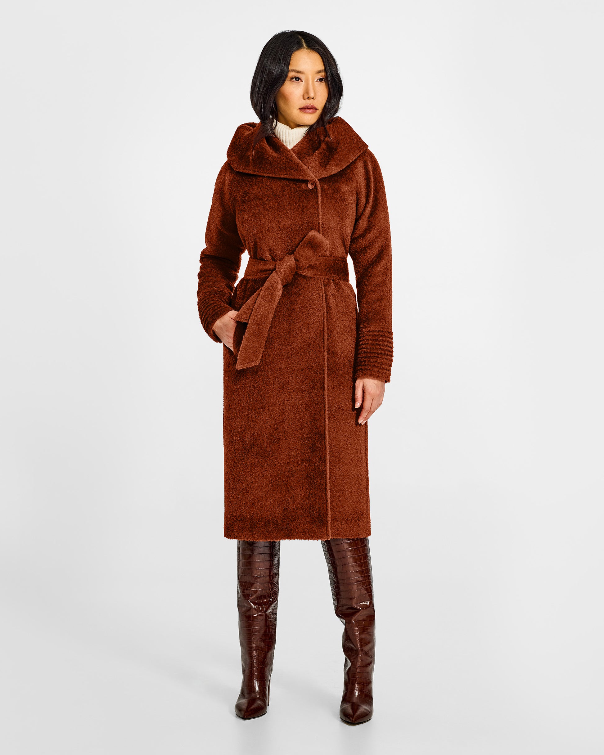 Front view of model wearing a Sentaler long rust brown coat made of bouclé alpaca wool, with a hooded collar, worn belted.