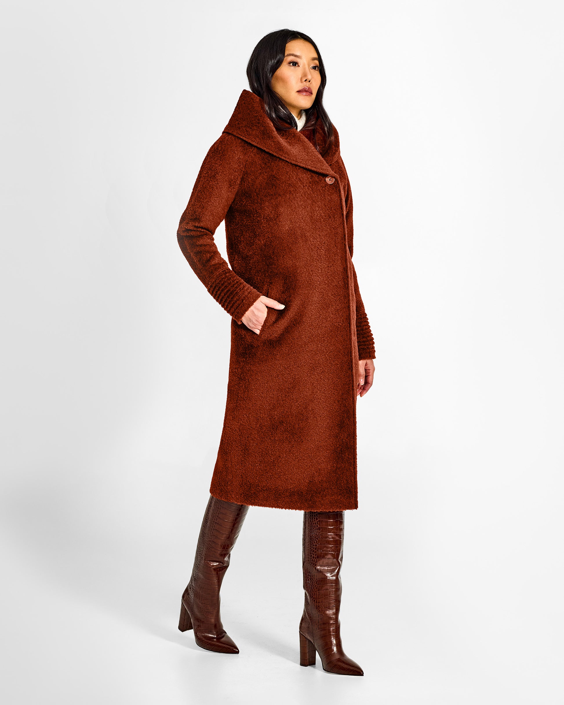 Side view of model wearing a Sentaler long rust brown coat made of bouclé alpaca wool, with a hooded collar, worn buttoned.