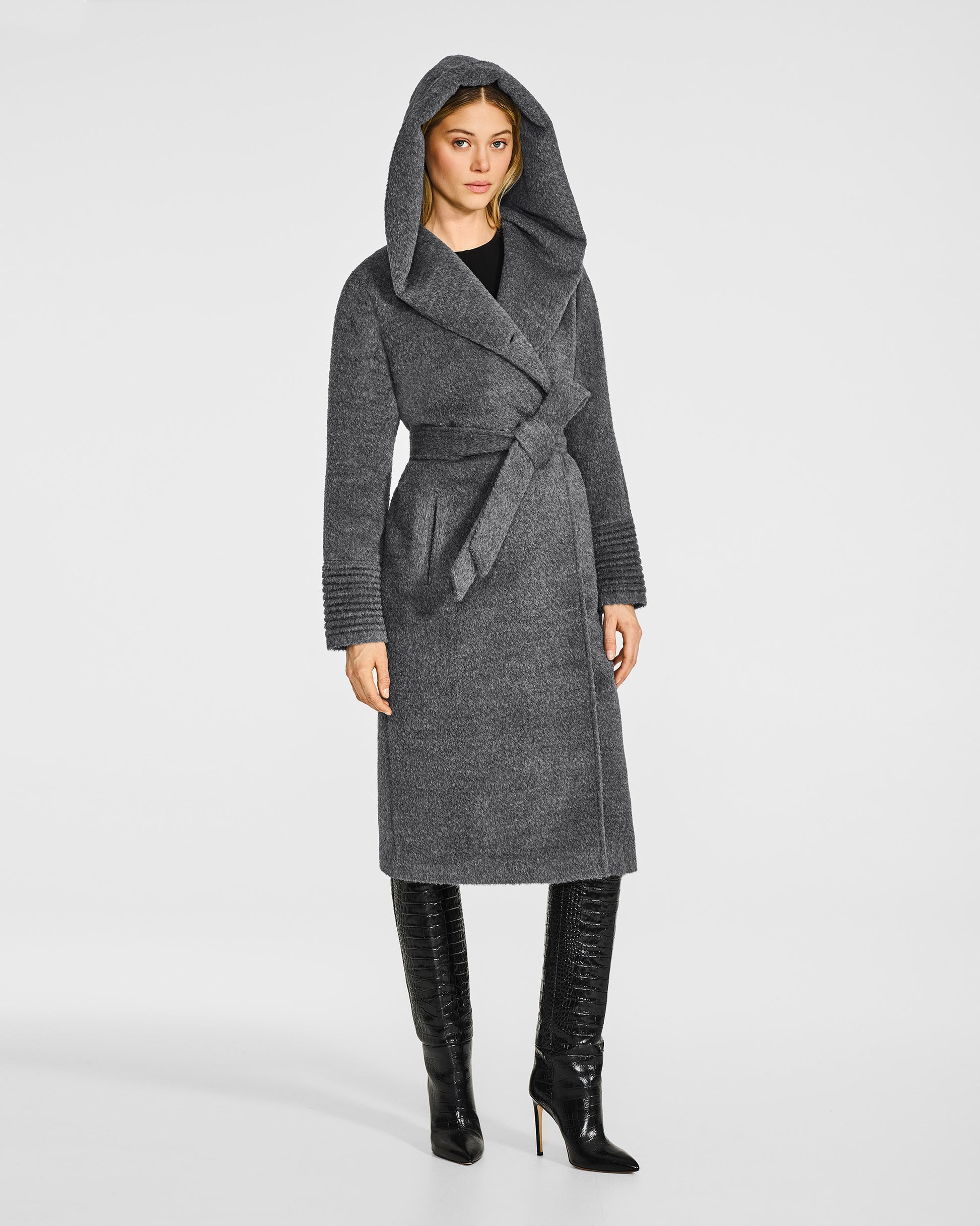 Side view of model wearing a Sentaler long grey mélange coat made of bouclé alpaca wool, with a hooded collar, worn belted.