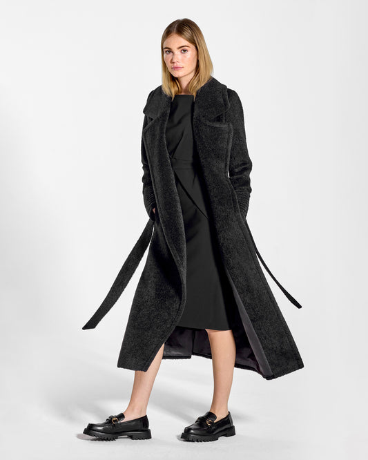 Side view of model wearing a Sentaler black wrap coat made of bouclé alpaca wool, with a notched collar, worn open.
