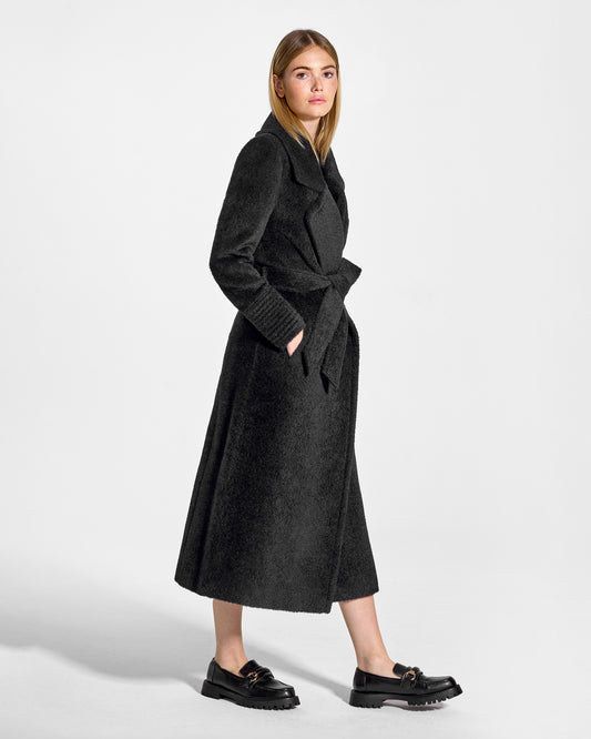 Side view of model wearing a Sentaler black wrap coat made of bouclé alpaca wool, with a notched collar, worn belted.