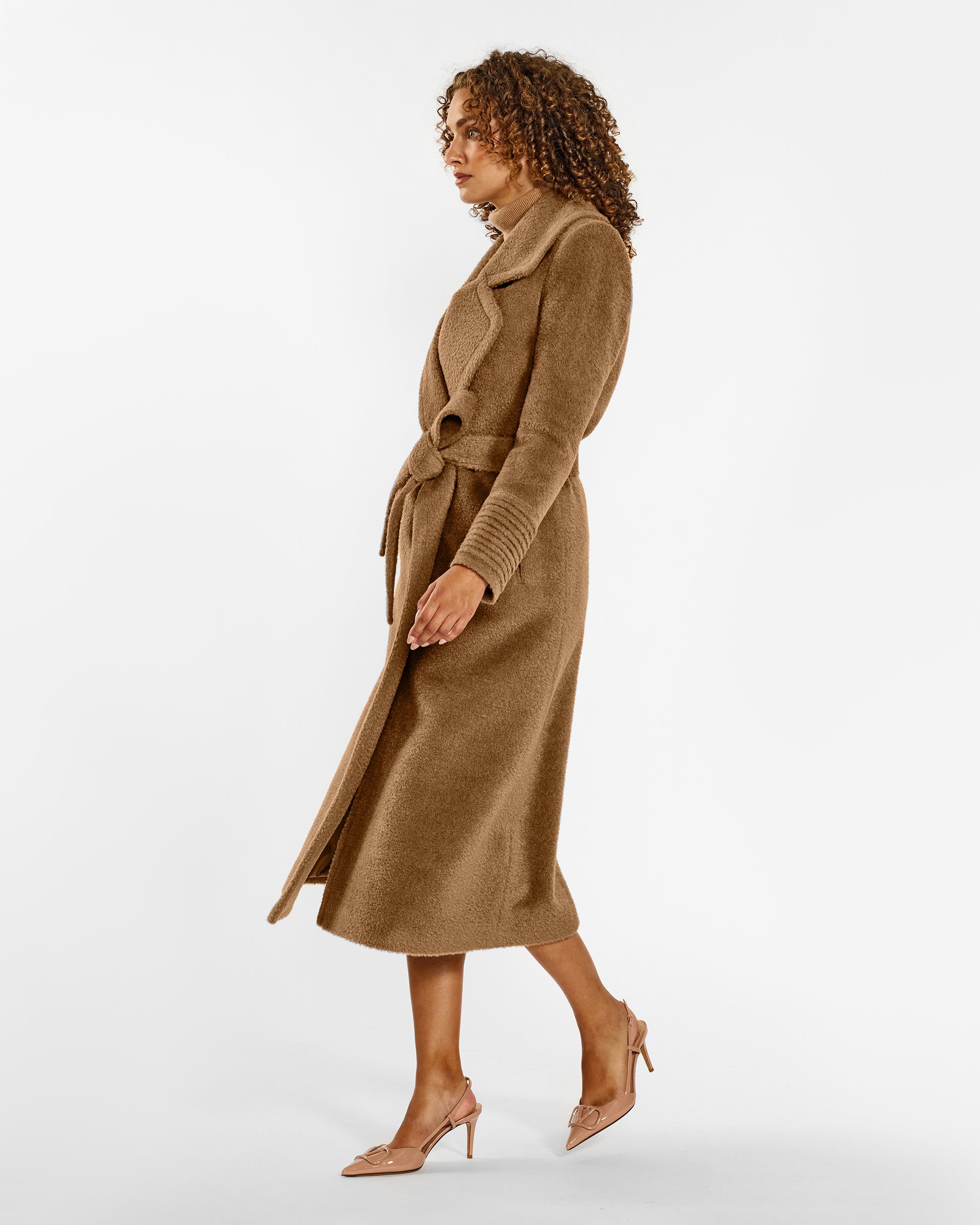 Side view of model wearing a Sentaler dark camel wrap coat made of bouclé alpaca wool, with a notched collar, worn belted.