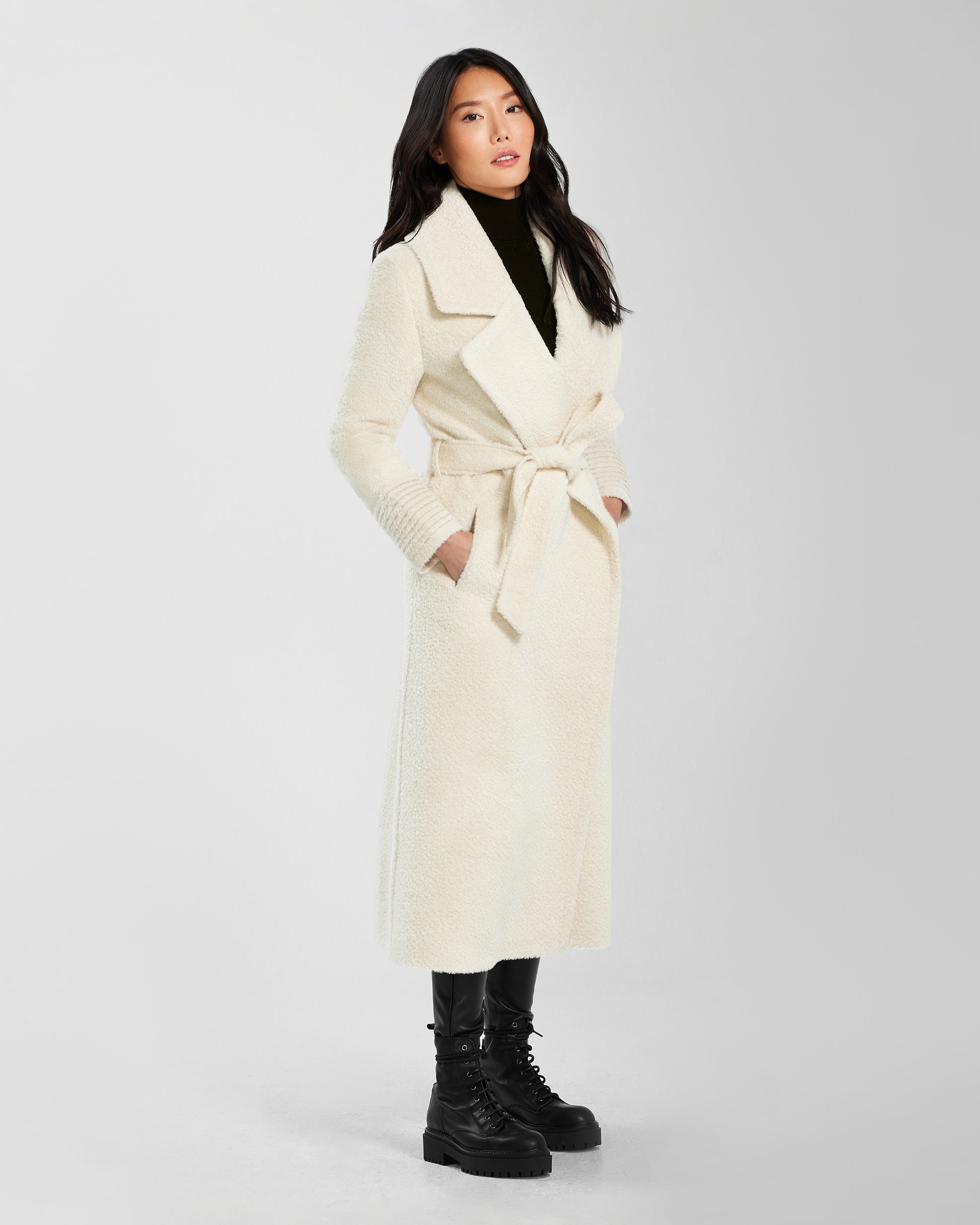 Side view of model wearing a Sentaler ivory wrap coat made of bouclé alpaca wool, with a notched collar, worn belted.