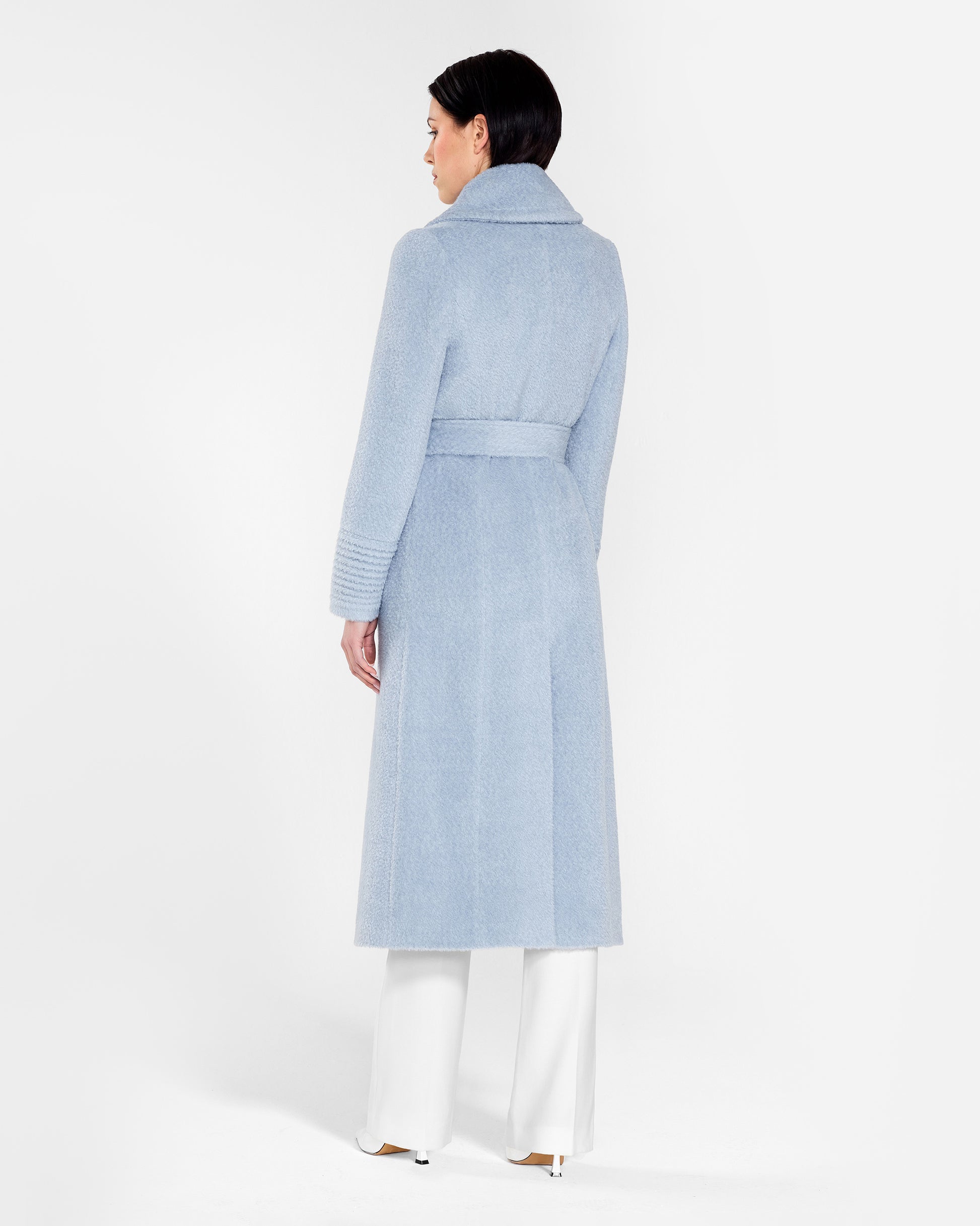 Back view of model wearing a Sentaler powder blue wrap coat made of bouclé alpaca wool, with a notched collar, worn belted.
