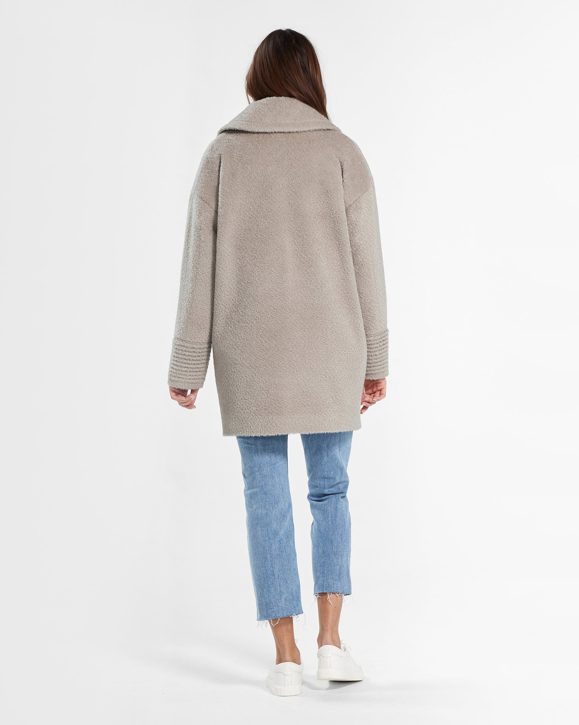 Back view of model wearing a Sentaler mid length sand oversized coat made of bouclé alpaca wool, worn buttoned.