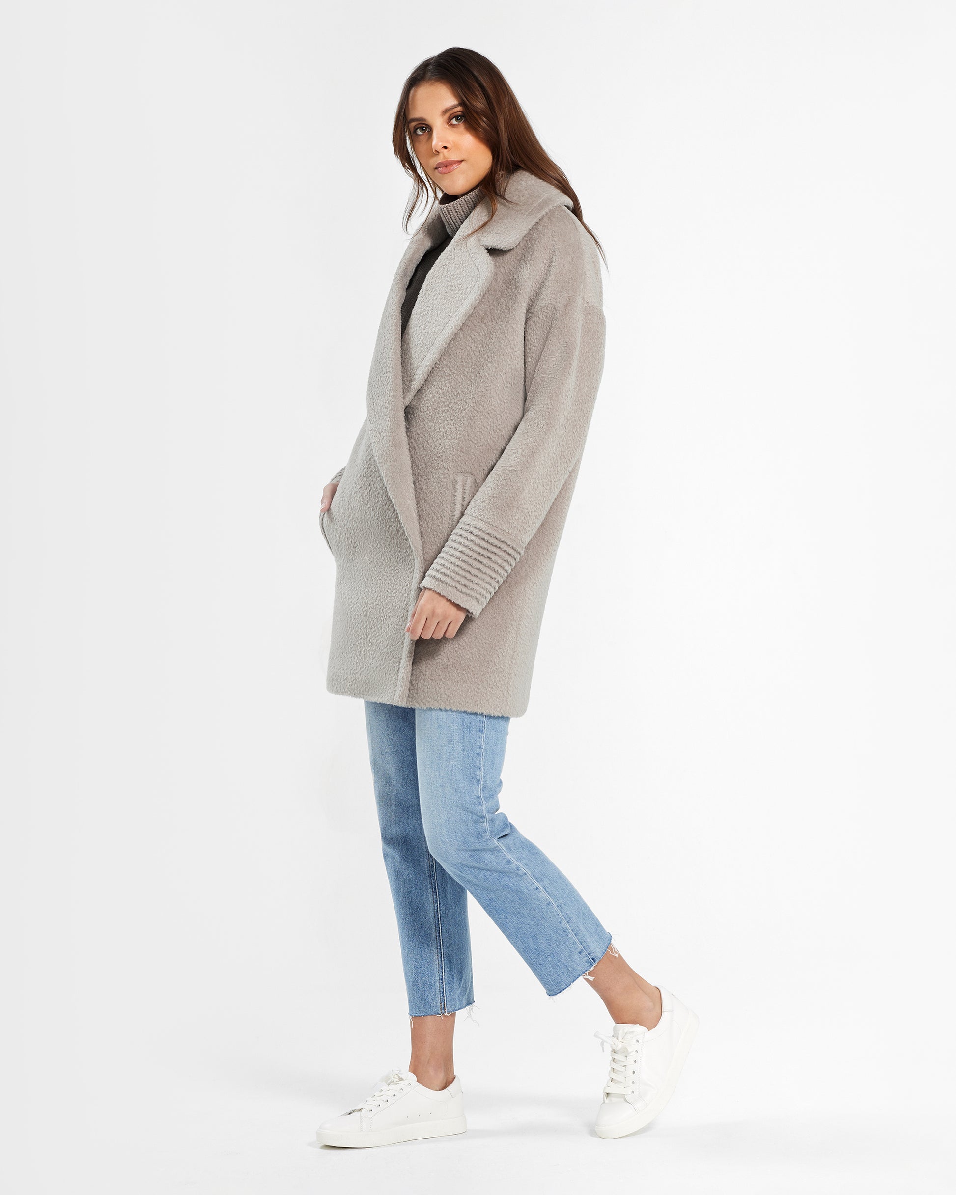 Side view of model wearing a Sentaler mid length sand oversized coat made of bouclé alpaca wool, worn buttoned.