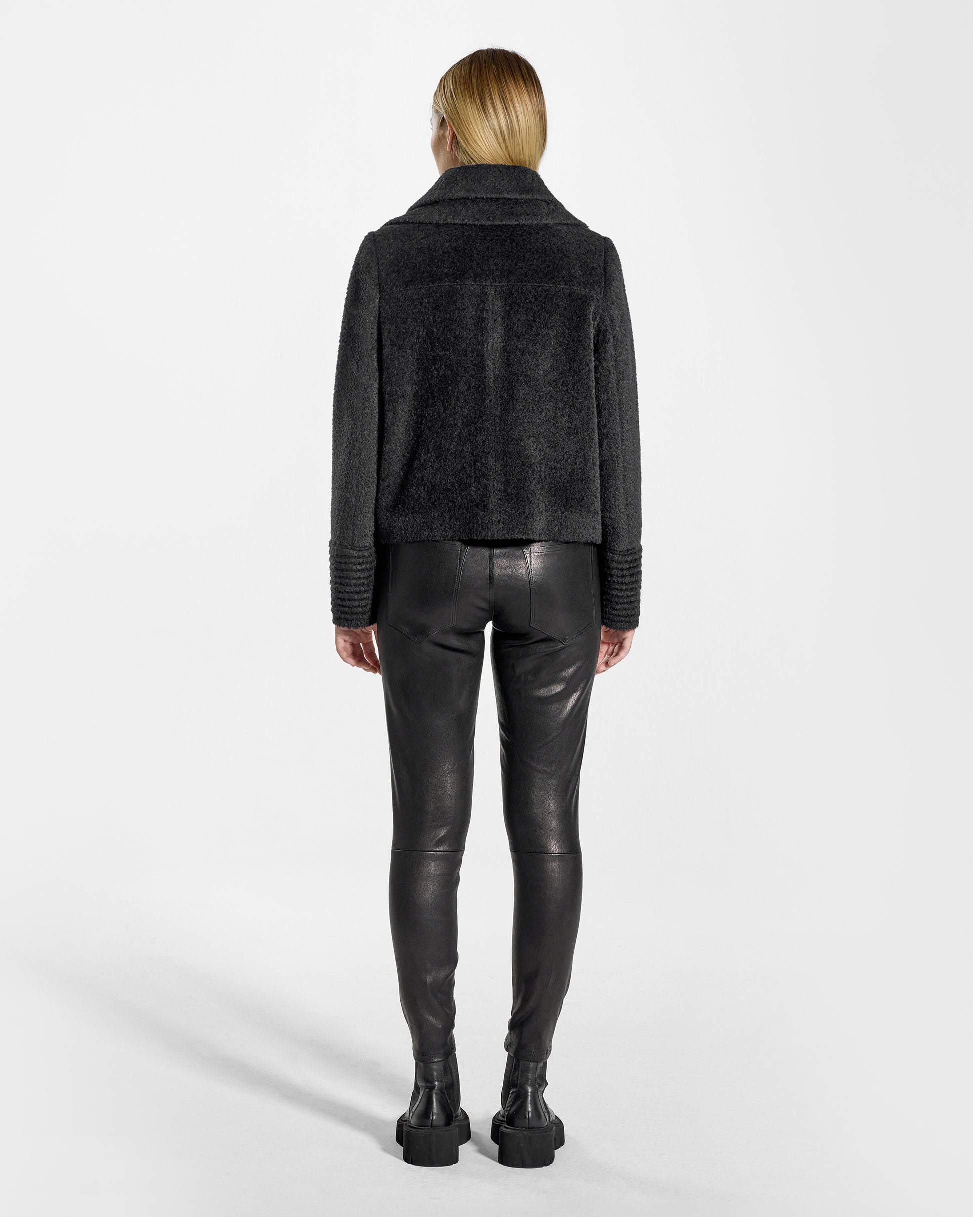 Back view of model wearing a Sentaler black moto jacket made of bouclé alpaca wool, with a double collar, worn buttoned.