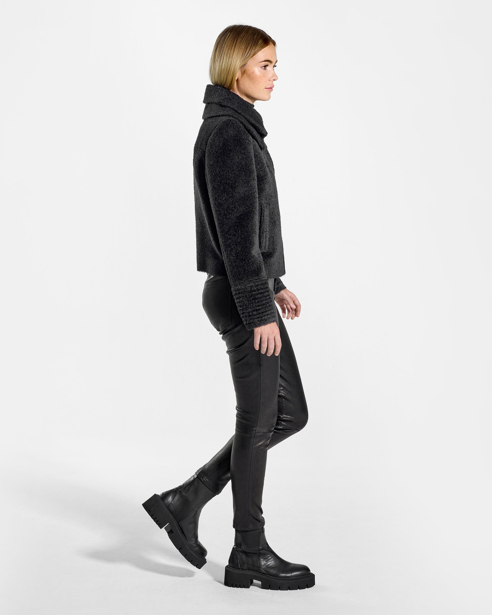 Side view of model wearing a Sentaler black moto jacket made of bouclé alpaca wool, with a double collar, worn buttoned.