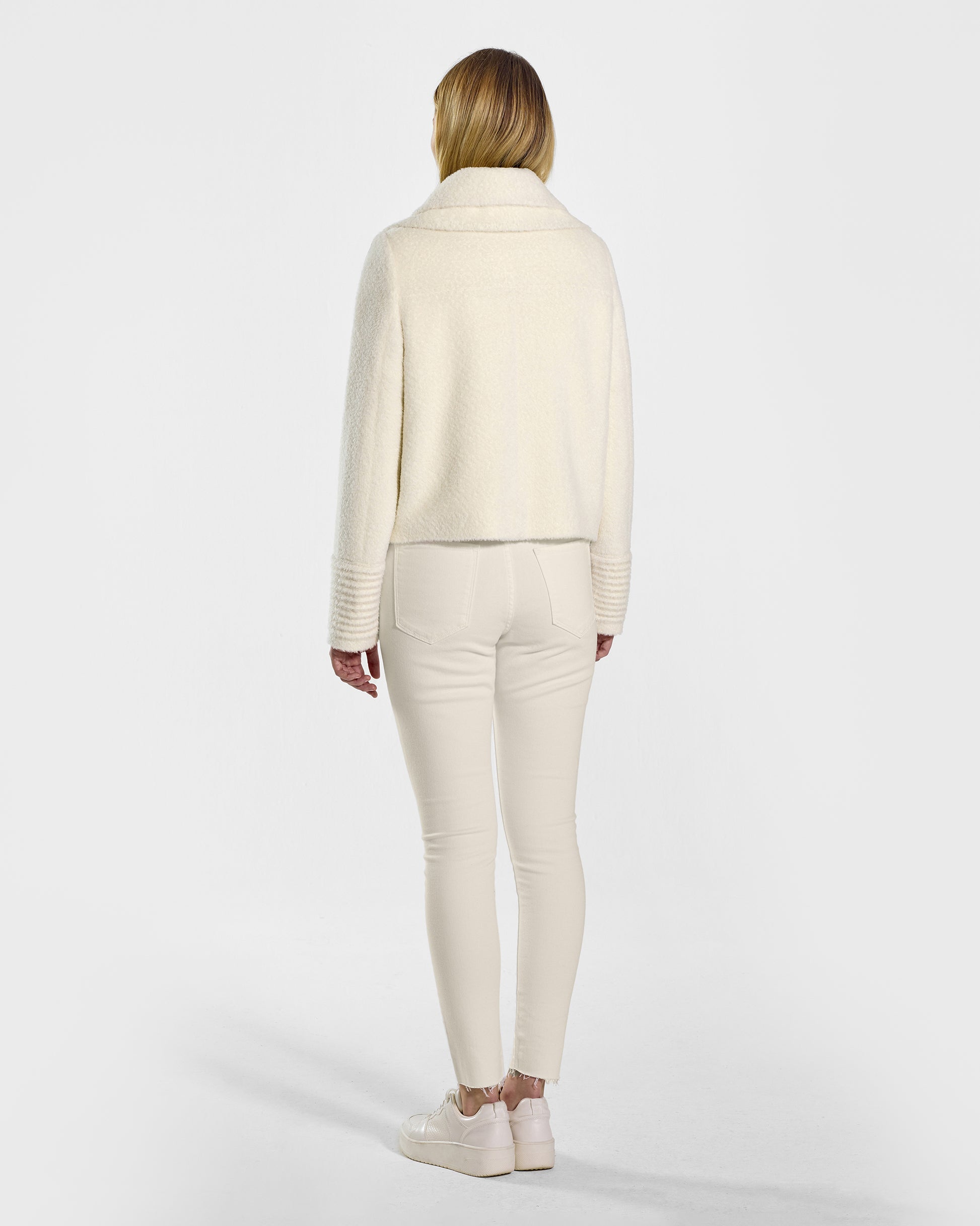 Back view of model wearing a Sentaler ivory moto jacket made of bouclé alpaca wool, with a double collar, worn buttoned.