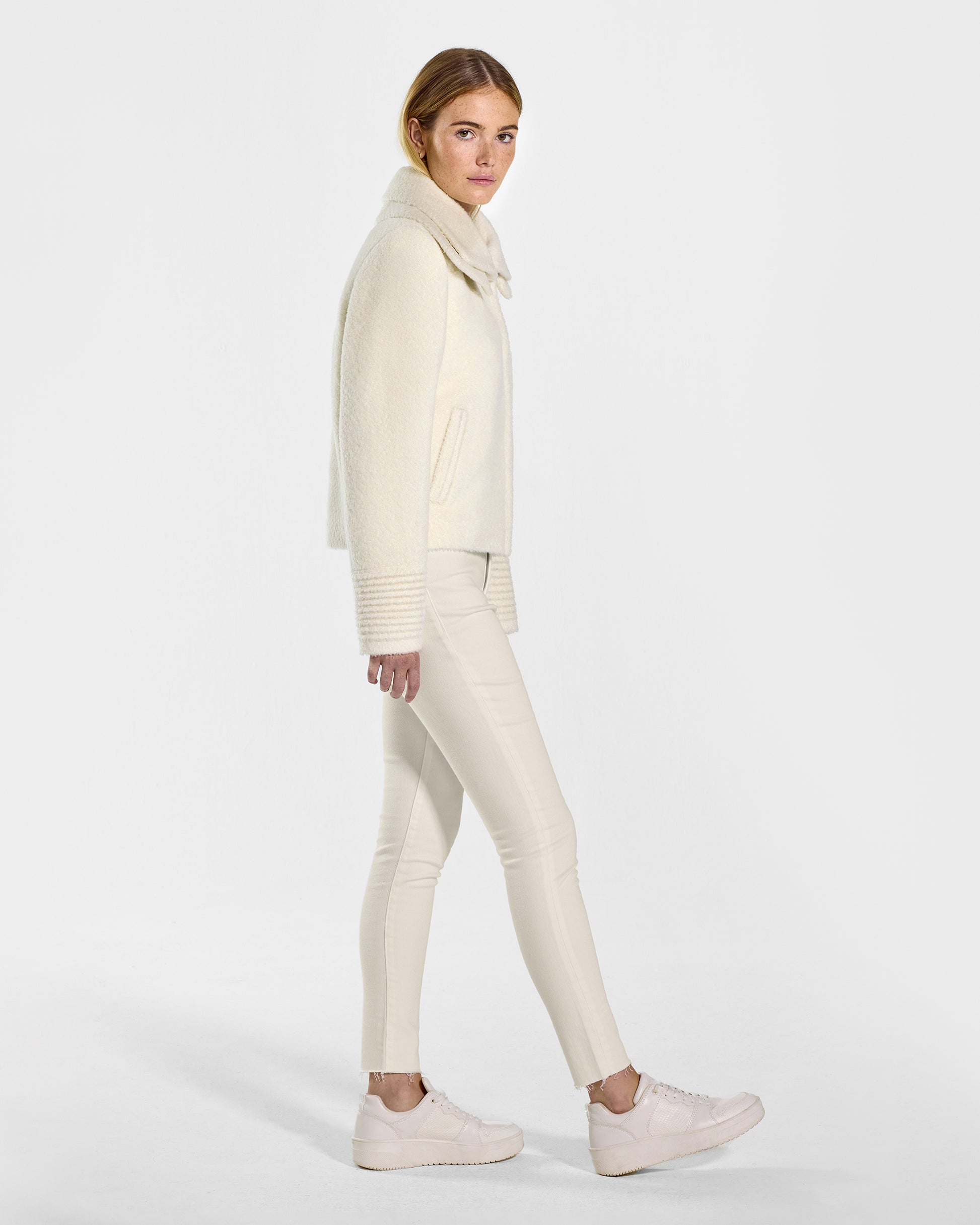Side view of model wearing a Sentaler ivory moto jacket made of bouclé alpaca wool, with a double collar, worn buttoned.