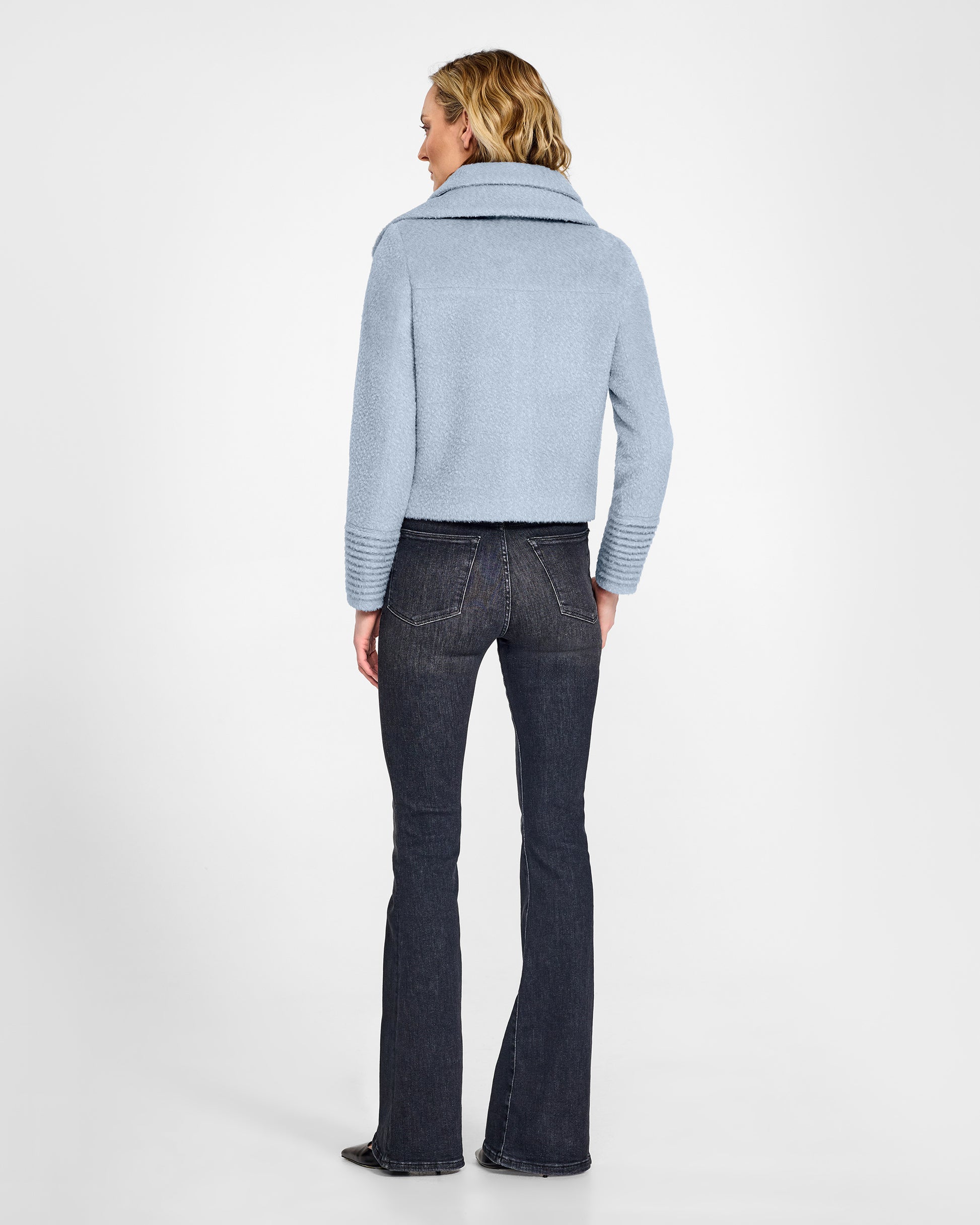 Back view of model wearing a Sentaler powder blue moto jacket made of bouclé alpaca wool, with a double collar, worn buttoned.