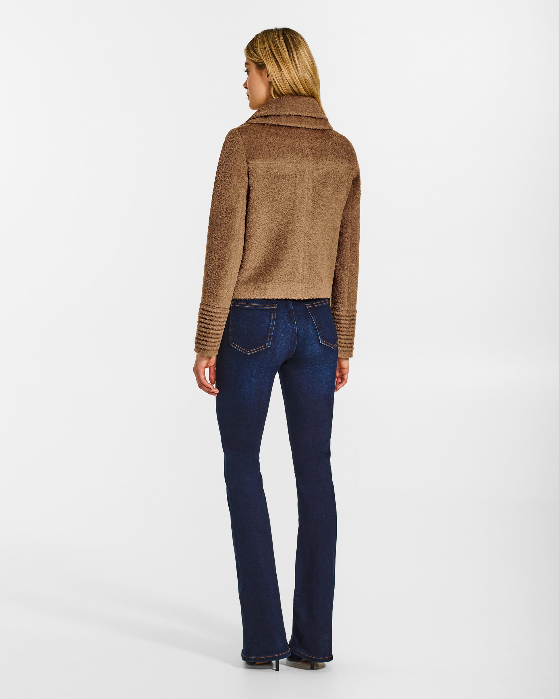 Back view of model wearing a Sentaler dark camel moto jacket made of bouclé alpaca wool, with a double collar, worn buttoned.