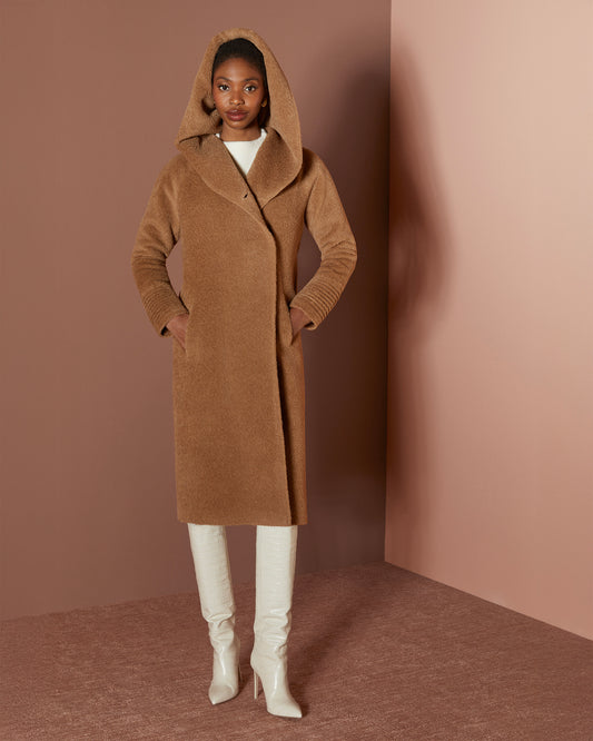 Front view of model wearing a Sentaler long dark camel coat made of bouclé alpaca wool, with a hooded collar, worn buttoned.