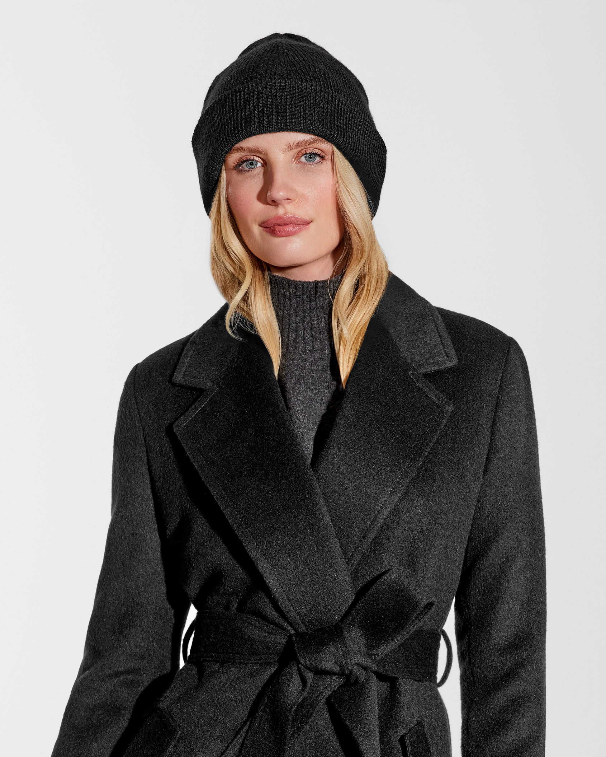 Front close up view of model wearing Sentaler's classic black beanie, made of baby alpaca yarn, paired with a black coat.