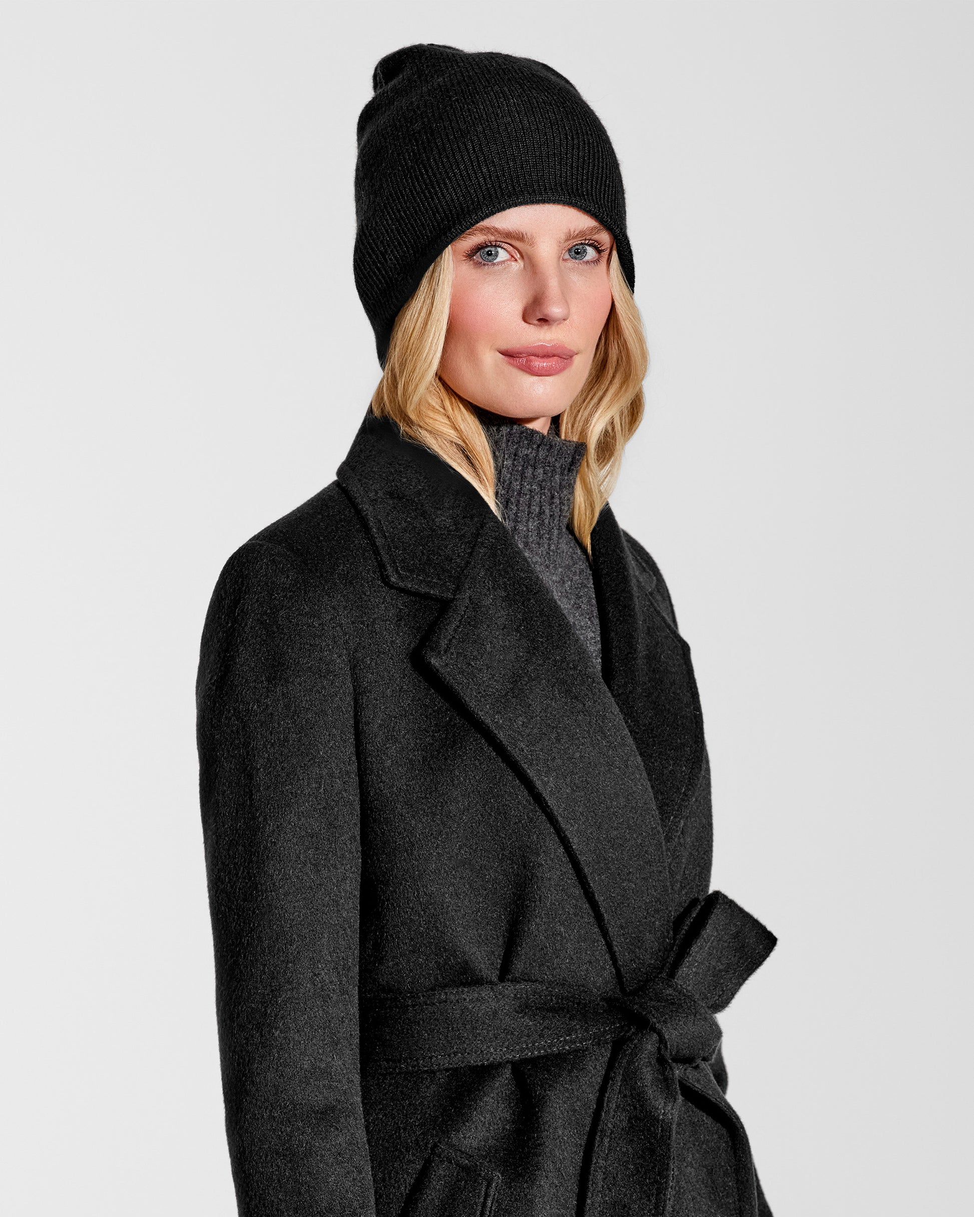 Side close up view of model wearing Sentaler's classic black beanie, made of baby alpaca yarn, paired with a black coat.