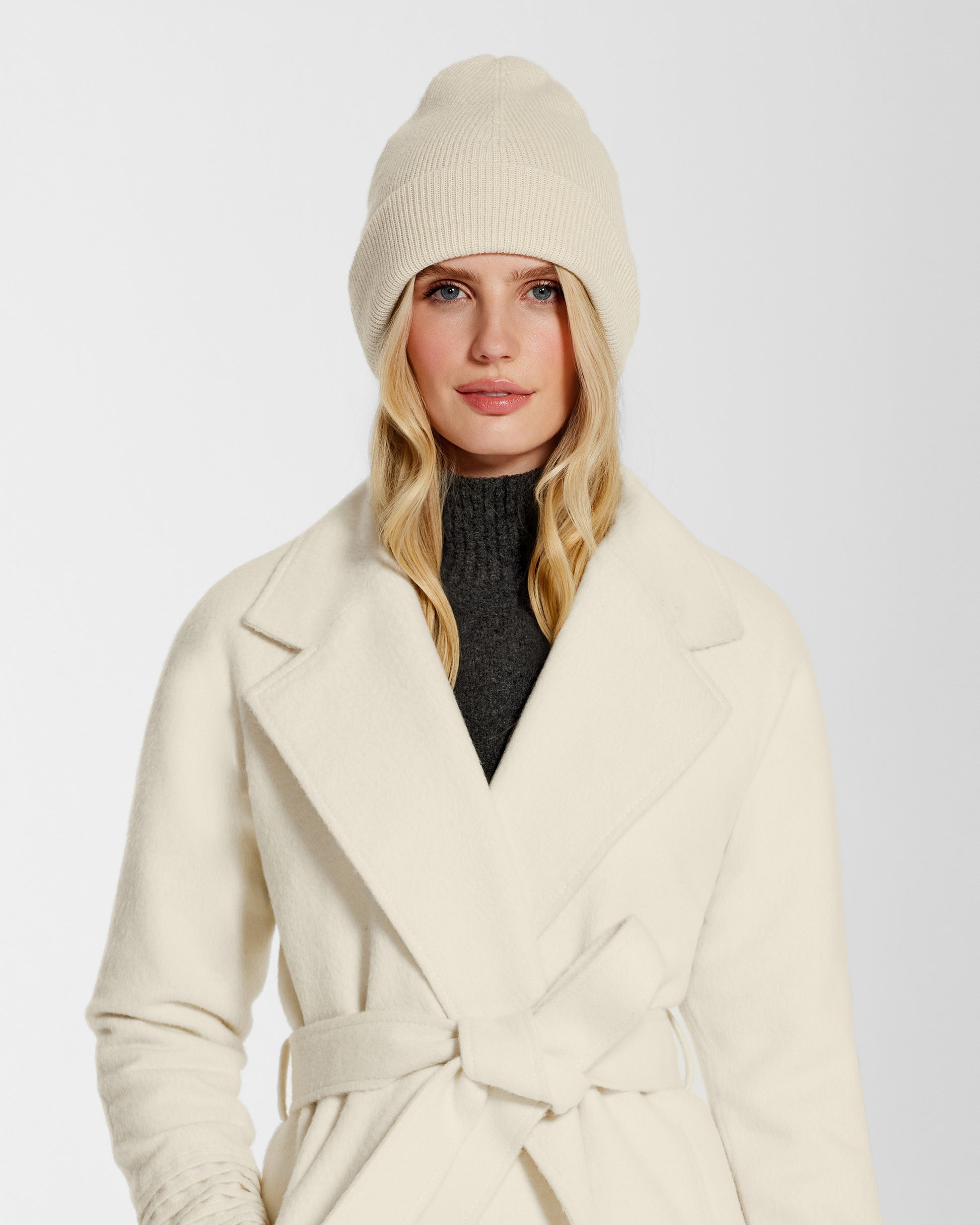 Front close up view of model wearing Sentaler's classic ivory beanie, made of baby alpaca yarn, paired with an ivory coat.