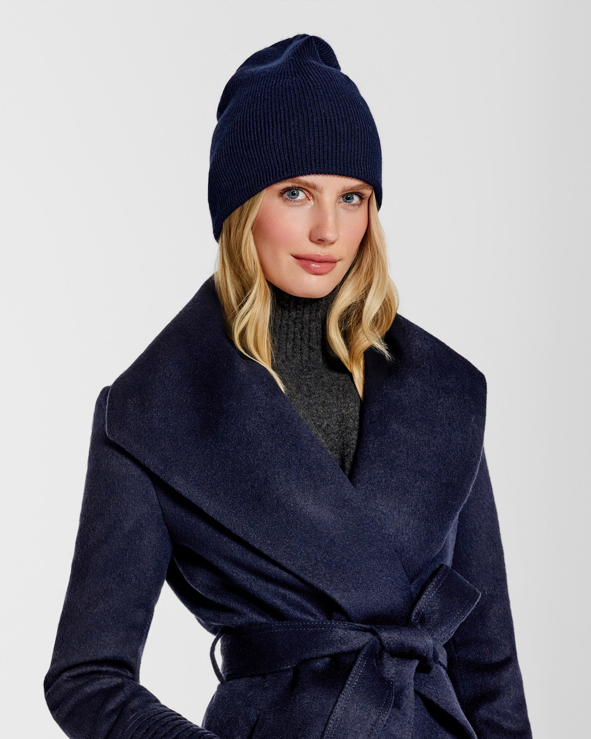 Front close up view of model wearing Sentaler's classic navy beanie, made of baby alpaca yarn, paired with a deep navy coat.