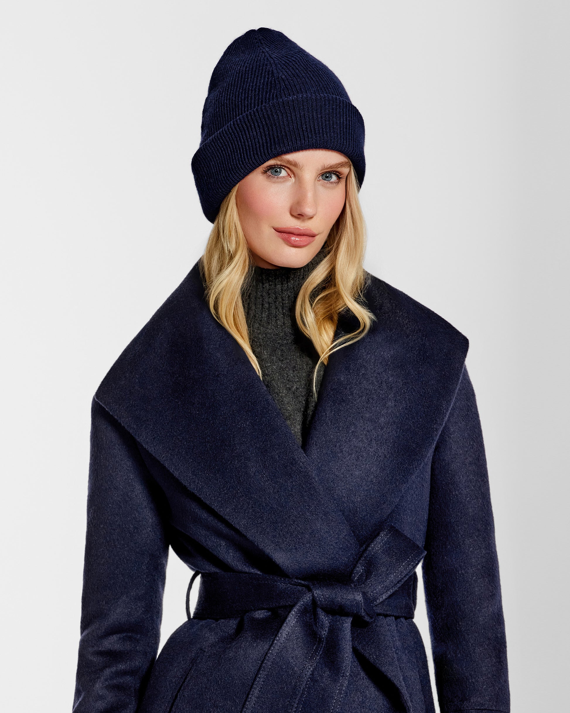 Front close up view of model wearing Sentaler's classic navy beanie, made of baby alpaca yarn, paired with a deep navy coat.