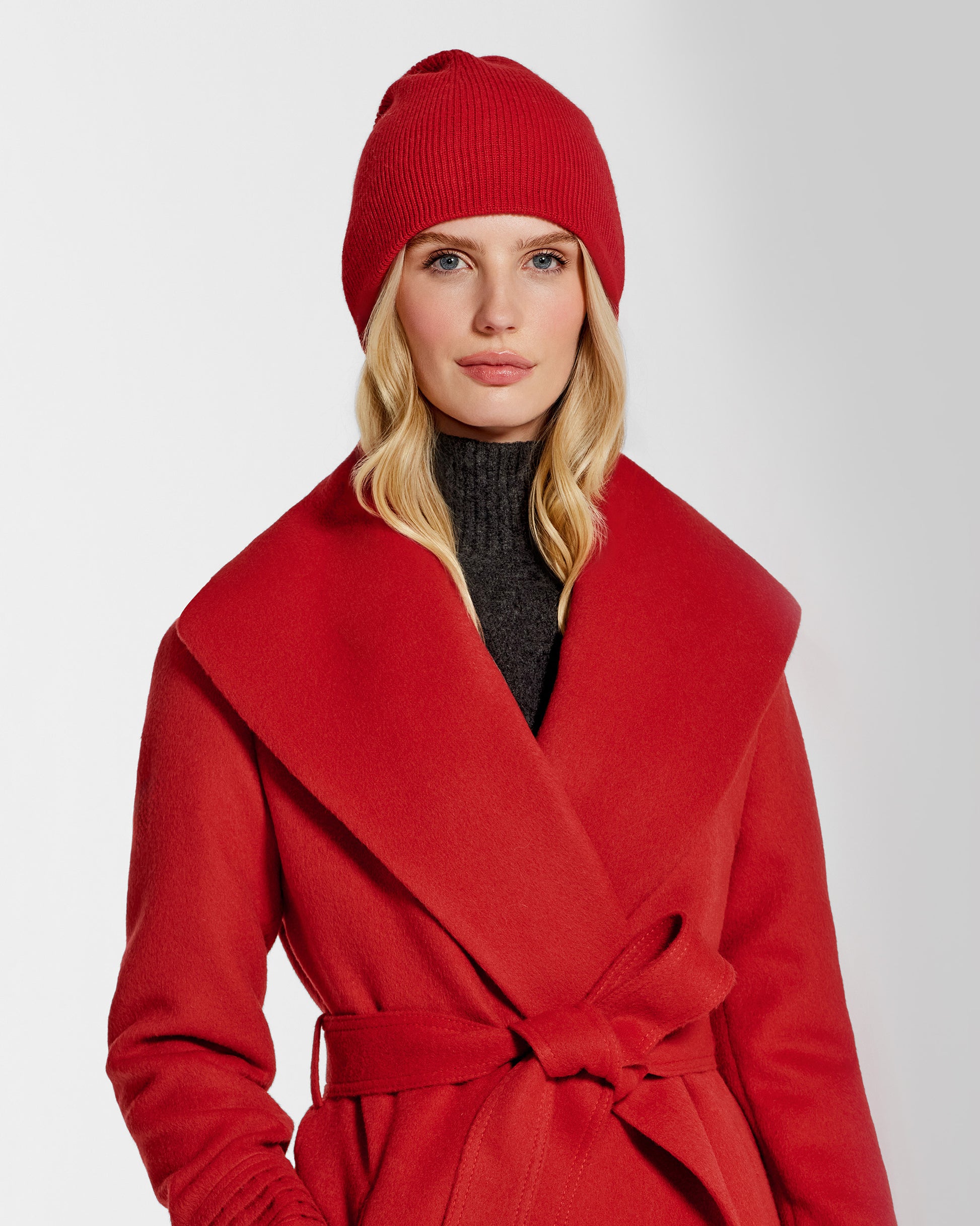 Front close up view of model wearing Sentaler's classic red beanie, made of baby alpaca yarn, paired with a scarlet red coat.