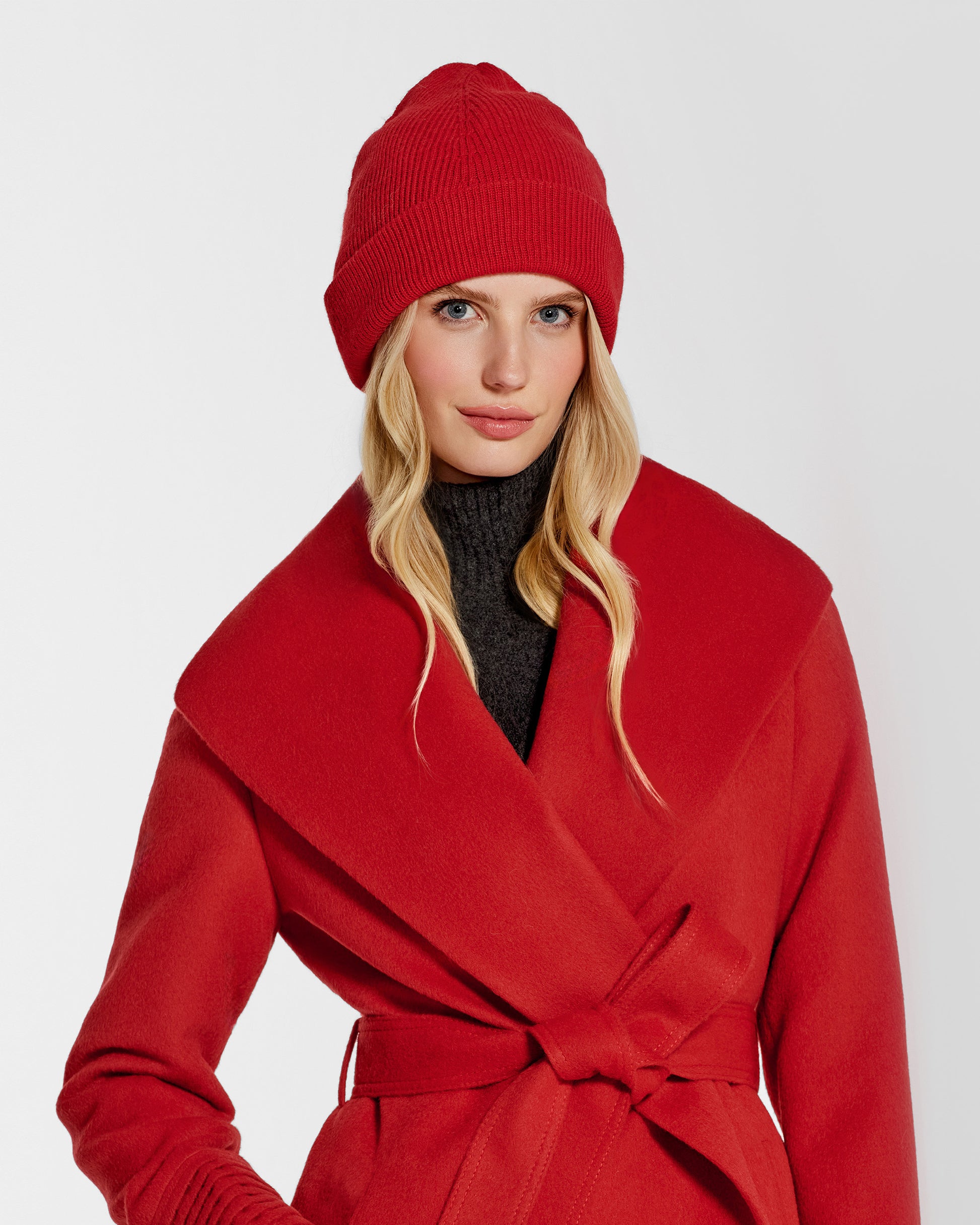 Front close up view of model wearing Sentaler's classic red beanie, made of baby alpaca yarn, paired with a scarlet red coat.
