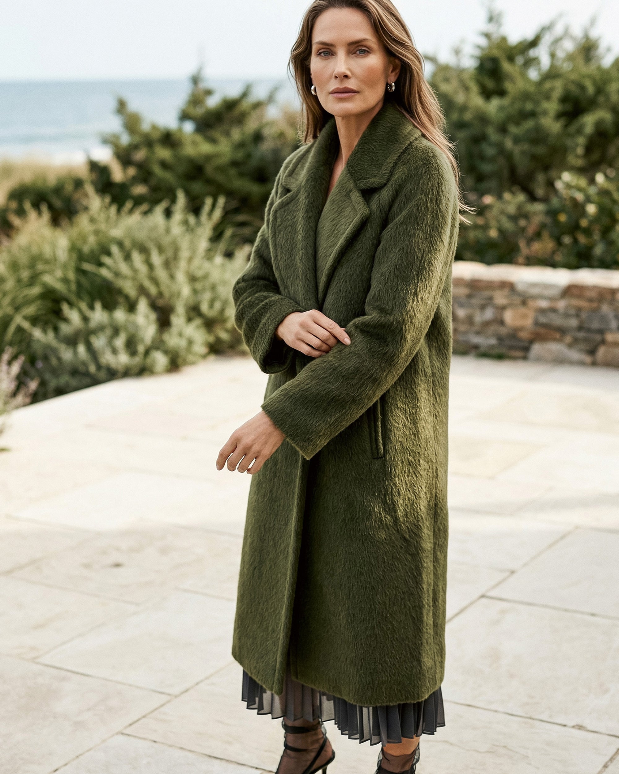 Front view of model wearing a Sentaler sea kelp green coat made of suri alpaca wool, with raglan sleeves, worn belted.