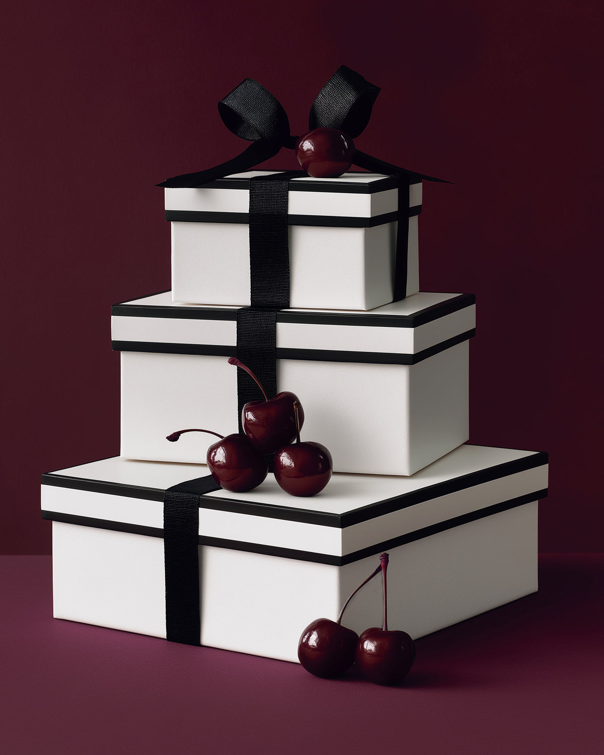 Three white gift boxes wrapped in black ribbon and accented with deep red cherries, styled against a rich burgundy backdrop for the SENTALER Gift Guide.