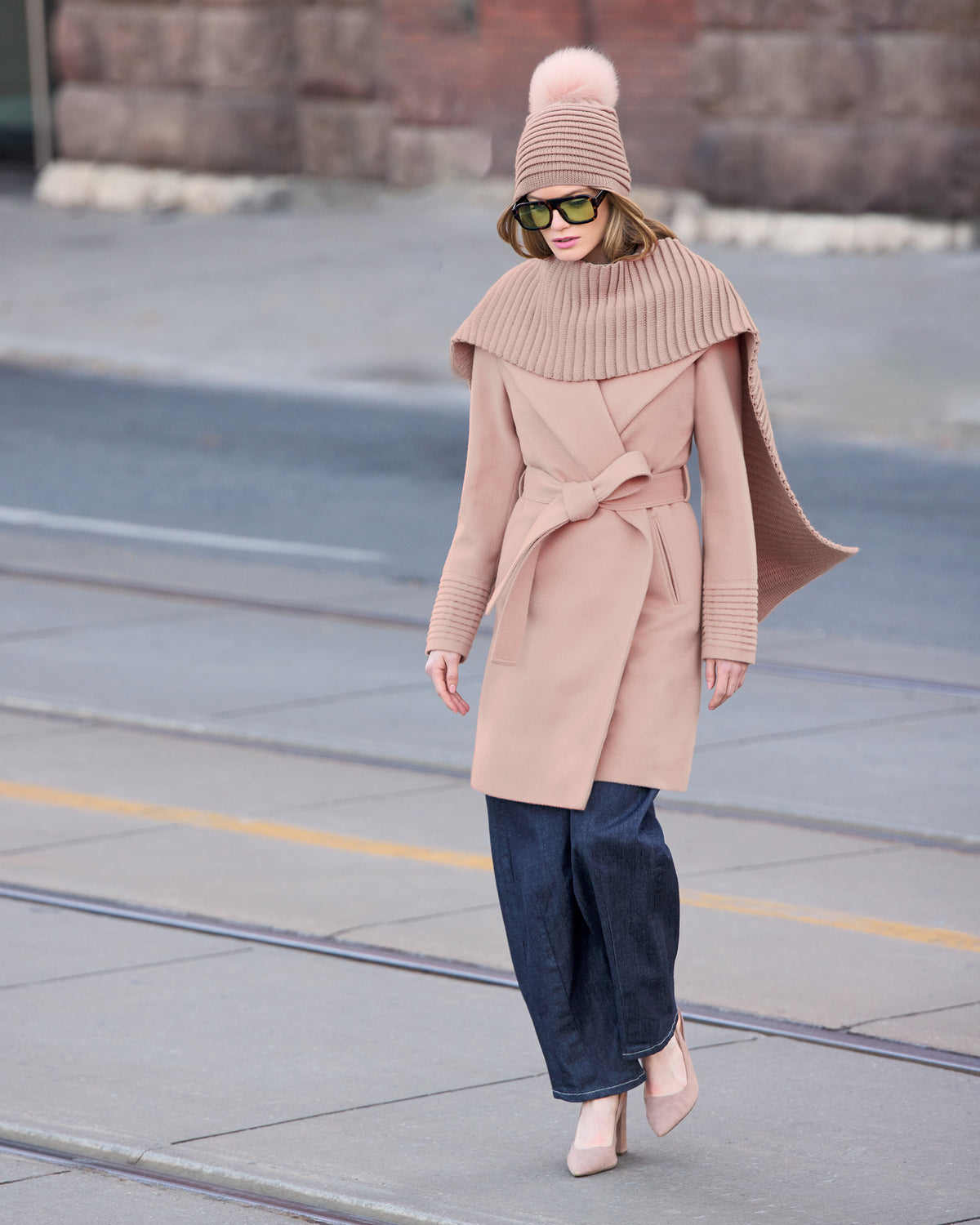 Front close up view of model wearing a Sentaler mid length blush pink coat made of baby alpaca wool, with a shawl collar, worn belted.