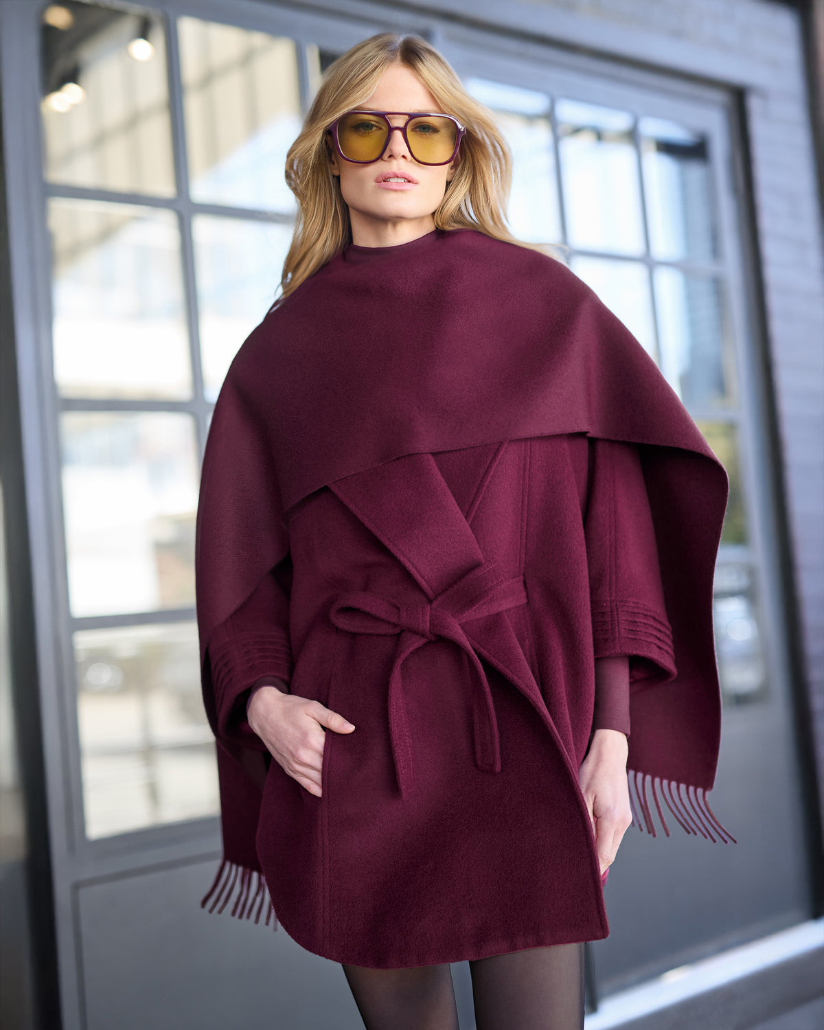 Front close up view of model wearing a Sentaler cherry lacquer cape made of baby alpaca wool, with a shawl collar, worn belted with matching cherry lacquer classic baby alpaca scarf.