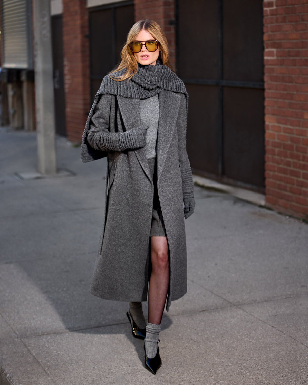 Front view of model wearing Sentaler's signature grey mélange ribbed hat, scarf, and gloves, paired with a matching grey mélange coat.